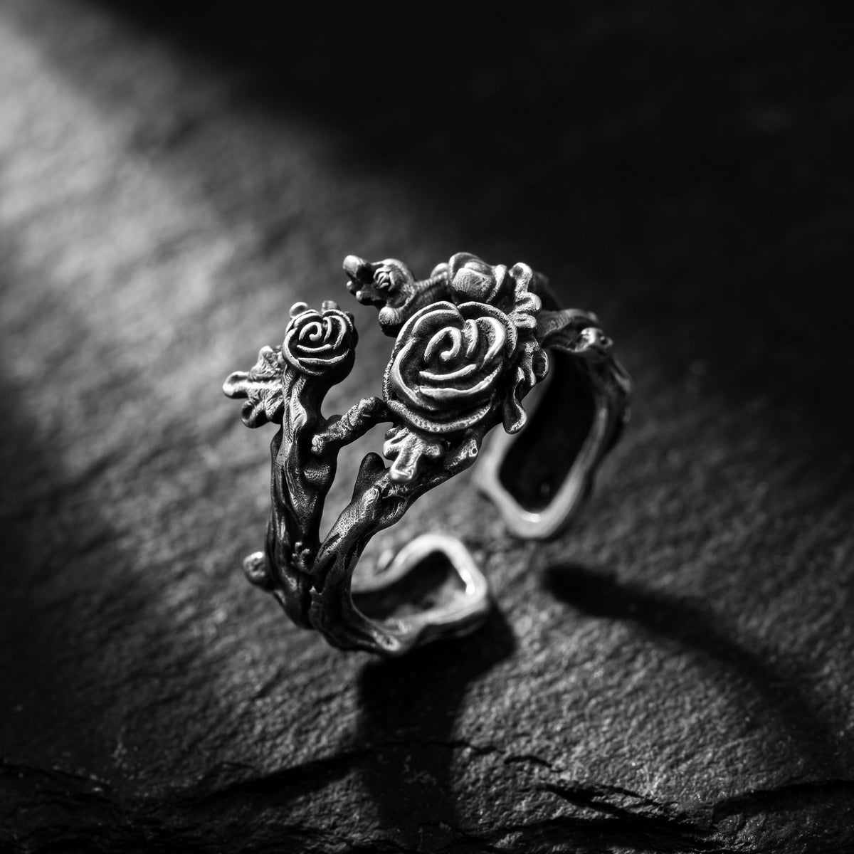 Close-up of the oxidized silver rose vine open ring on a dark slate surface, with carved roses and leaves.