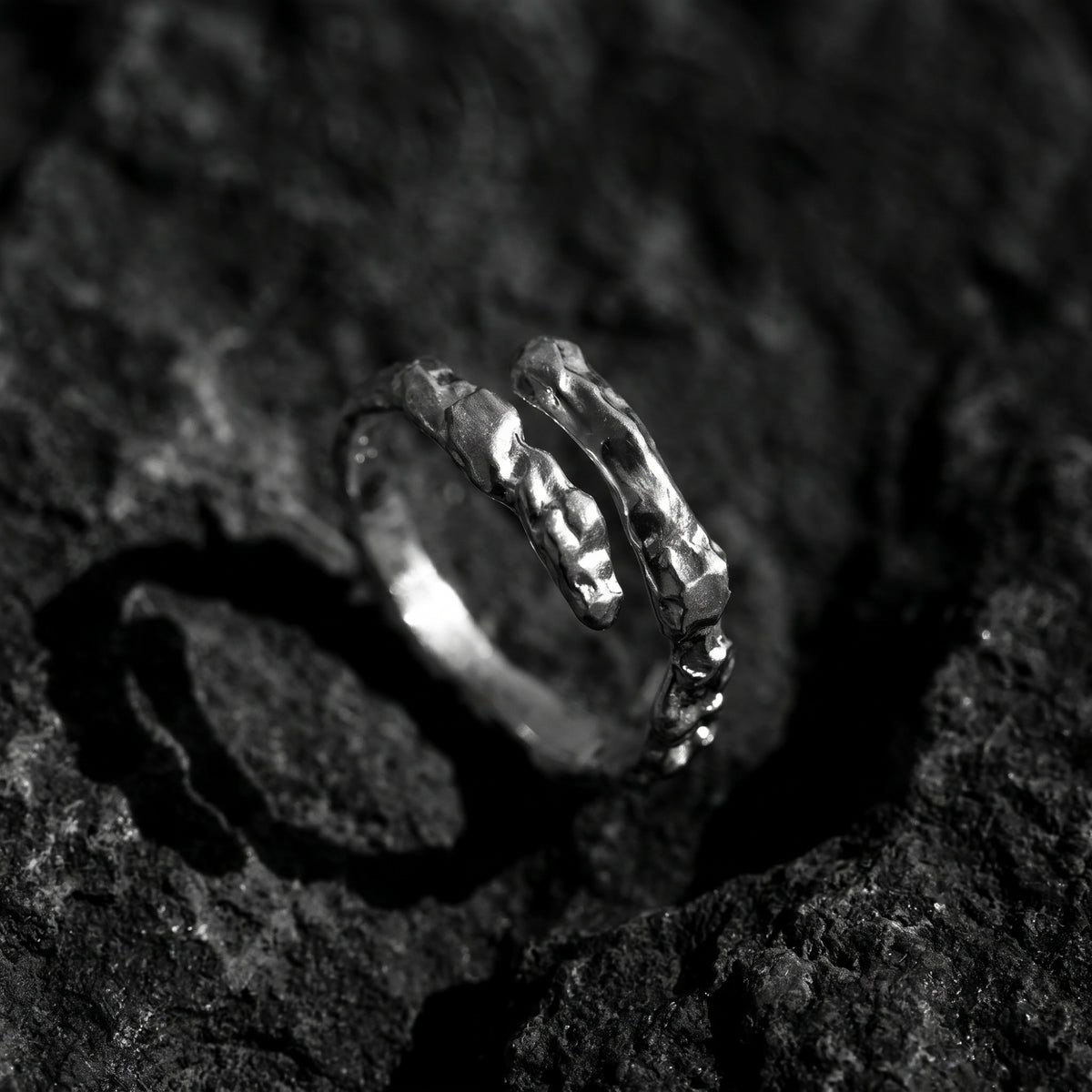 Silver molten-textured open bypass ring angled upright on a dark, rough stone surface.