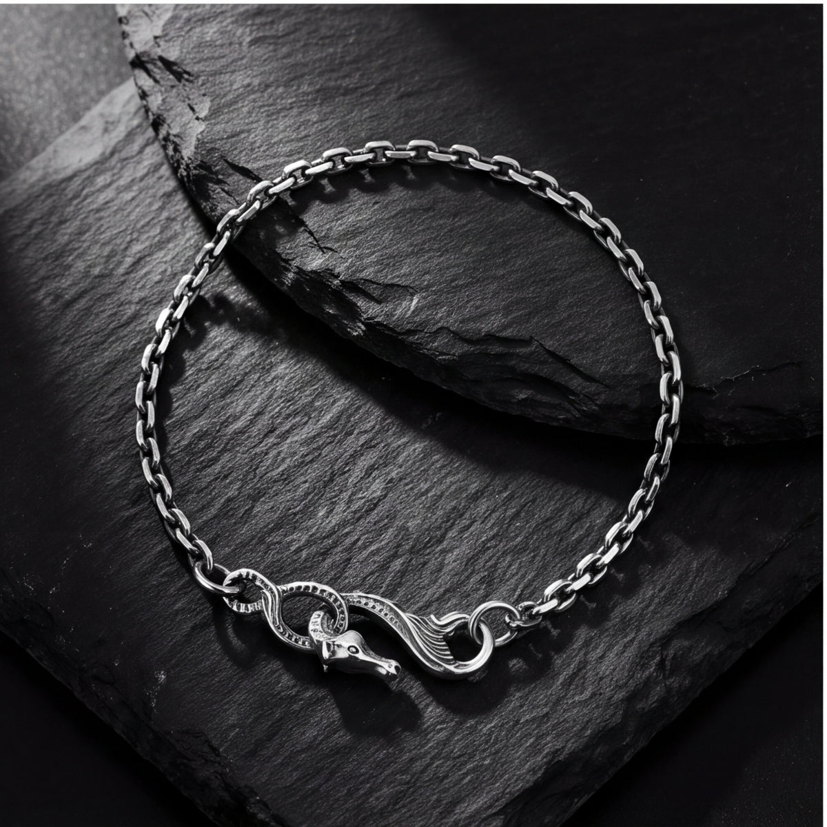 Top-down view of the silver dragon chain bracelet arranged in a loop on a dark slate surface.