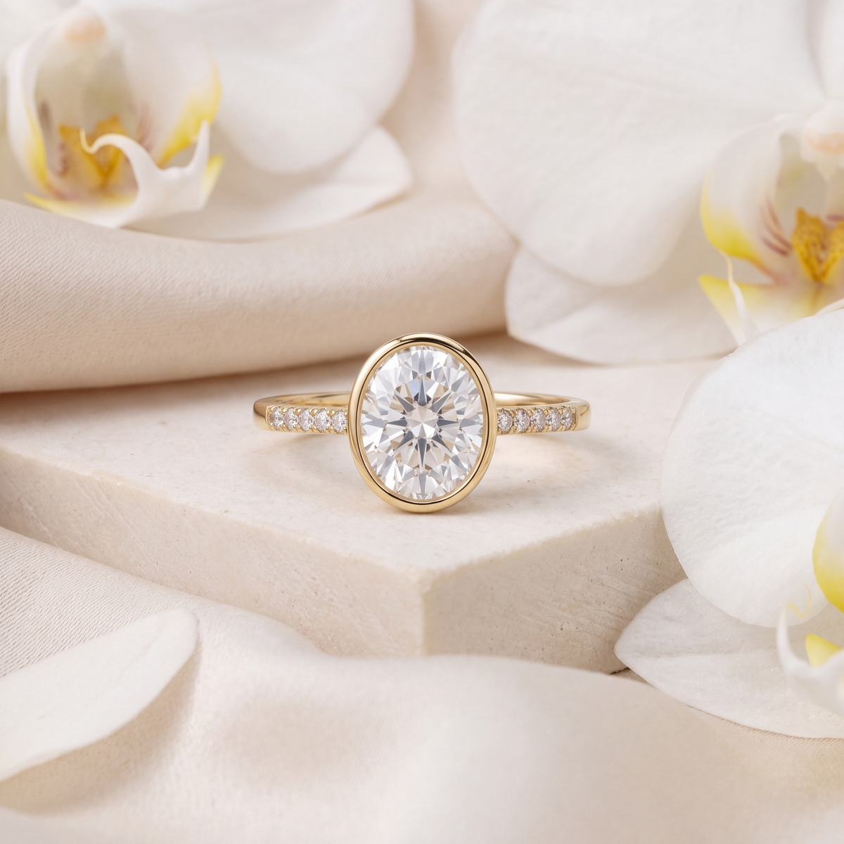 Yellow gold oval moissanite bezel engagement ring with a pavé band displayed on a stone surface.