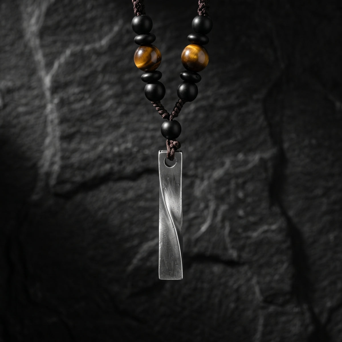 Twisted silver bar pendant necklace with tiger eye and black beads against a dark textured background.