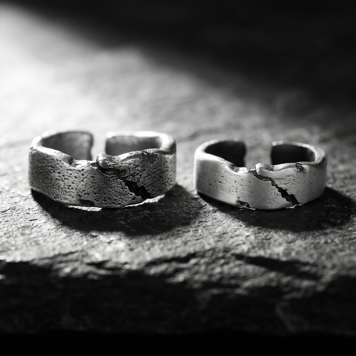 Two open silver Rift Fracture rings with textured fissures displayed side by side on a dark textured surface.