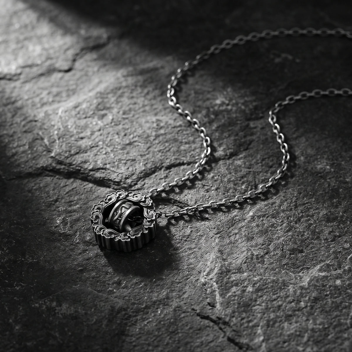 Silver cloud wheel pendant with carved cloud motifs and chain resting on dark stone.