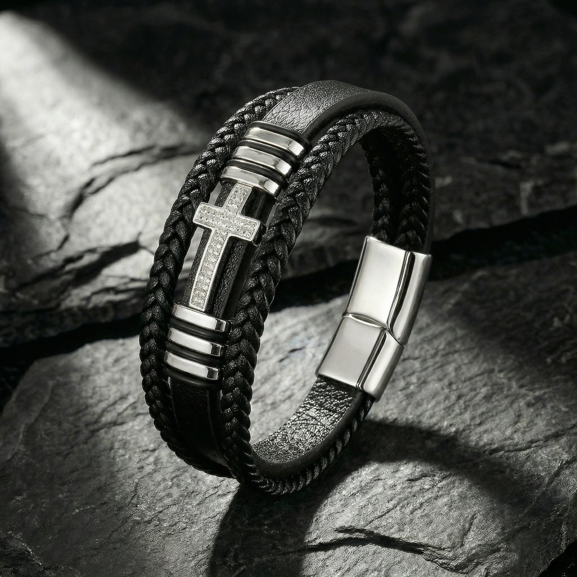 Aegis Cross Bracelet in black braided leather and stainless steel with pavé stones on a dark stone background.
