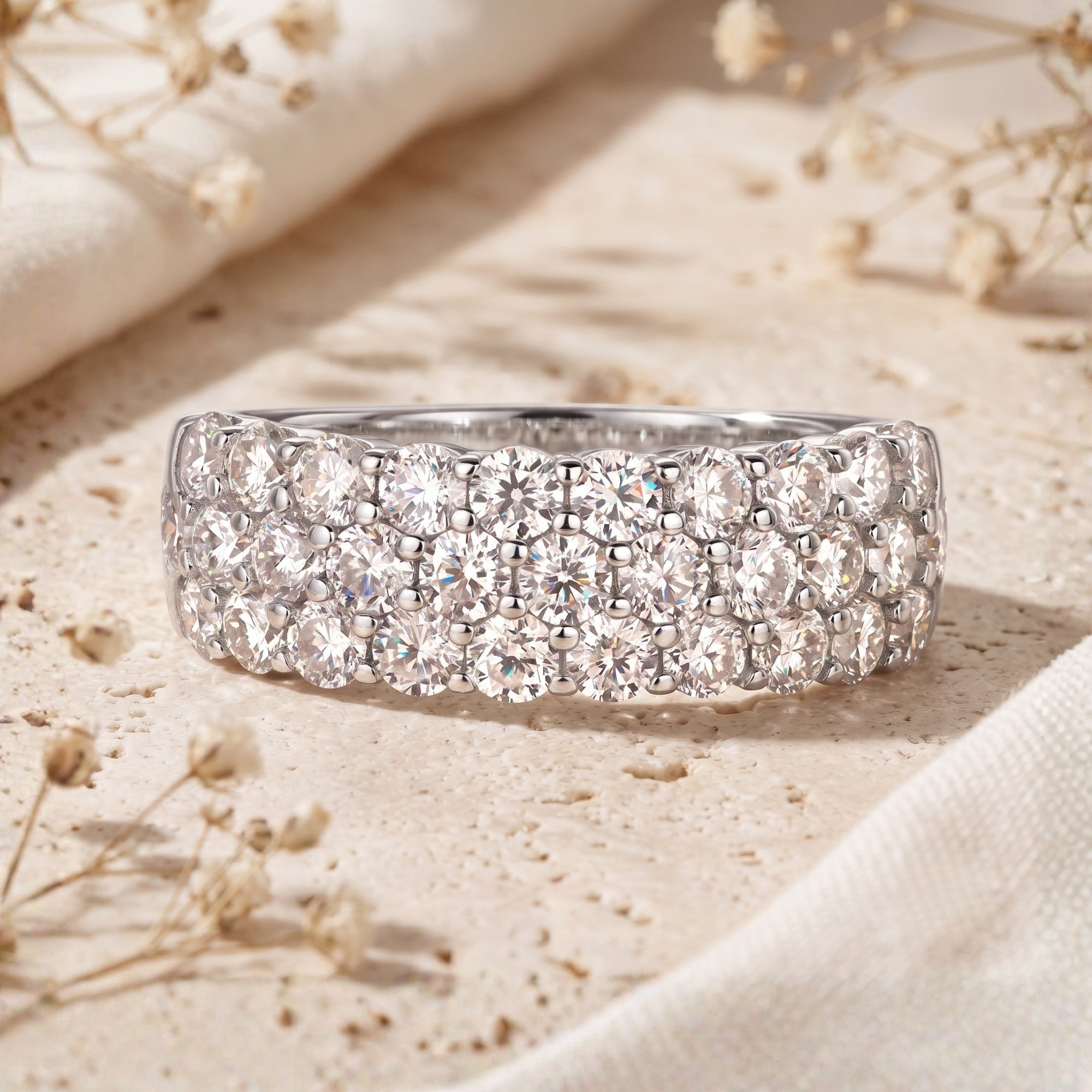 Three-row round cubic zirconia pavé ring in S925 sterling silver on a stone surface.