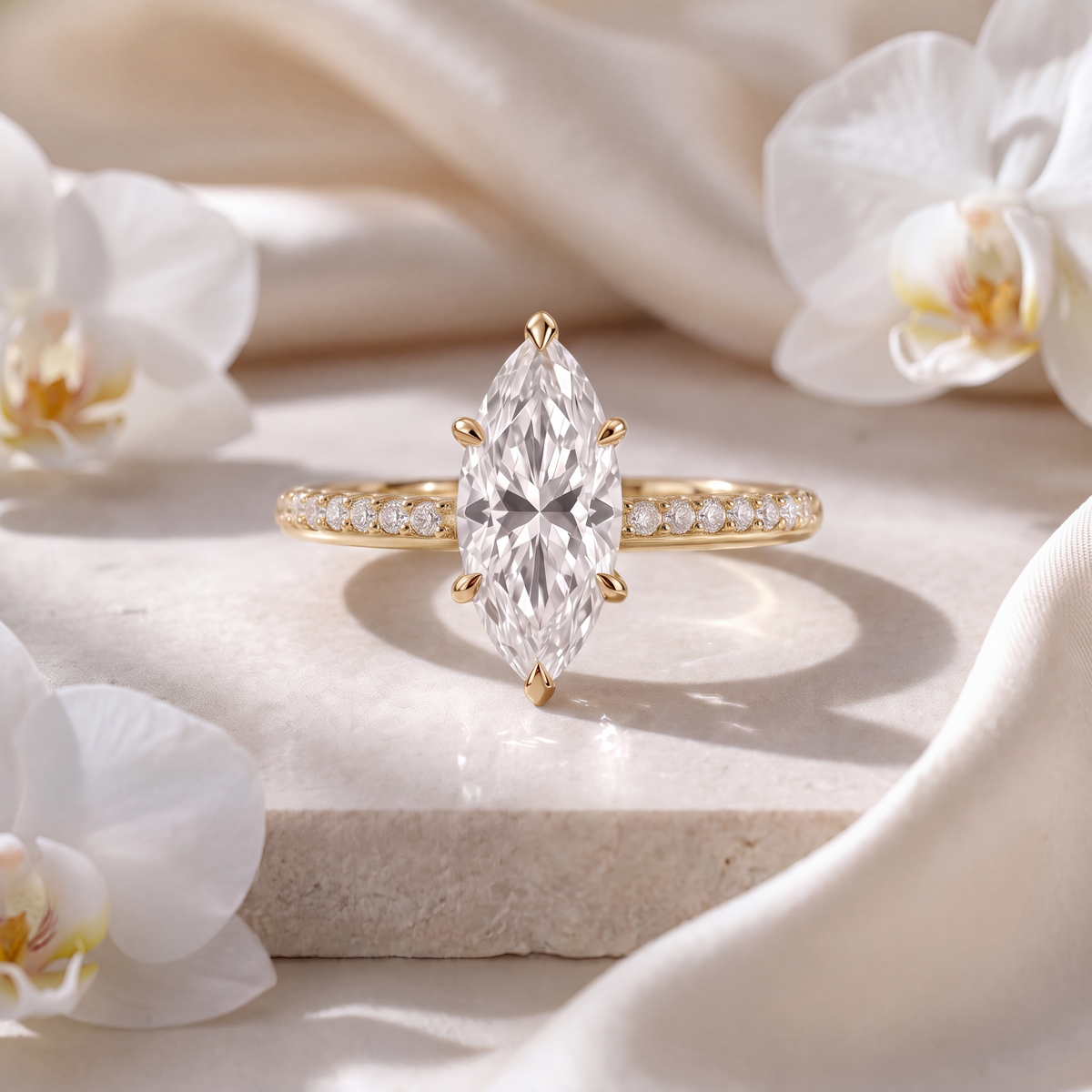 Yellow gold marquise moissanite engagement ring with a pavé band set on a stone slab.