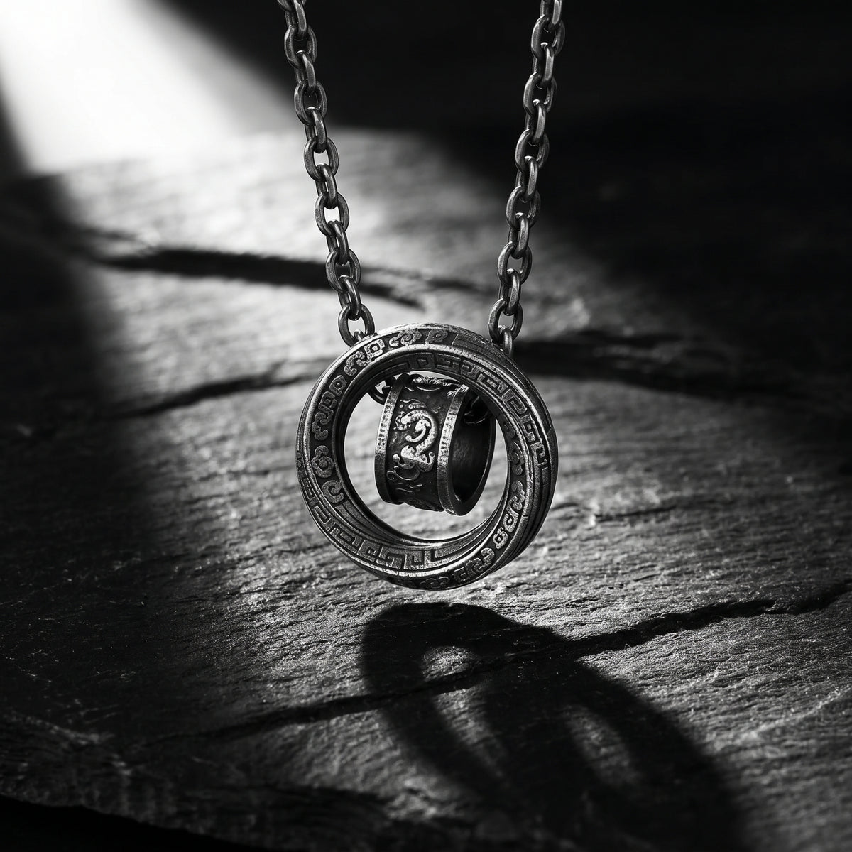 Close-up of the double-ring pendant hanging from its chain above layered slate stones.