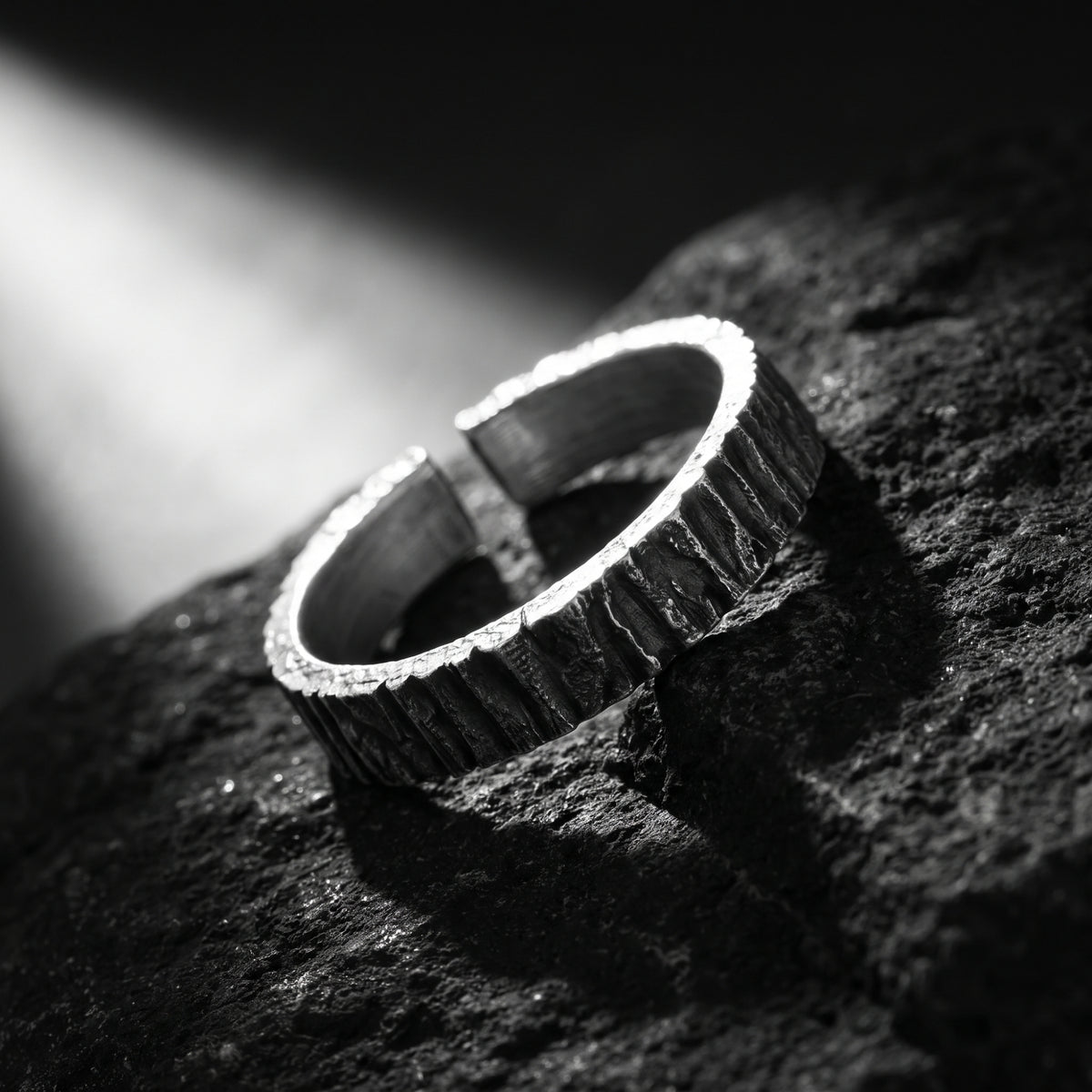 Textured silver bark open band ring angled on dark rock under dramatic spotlight.