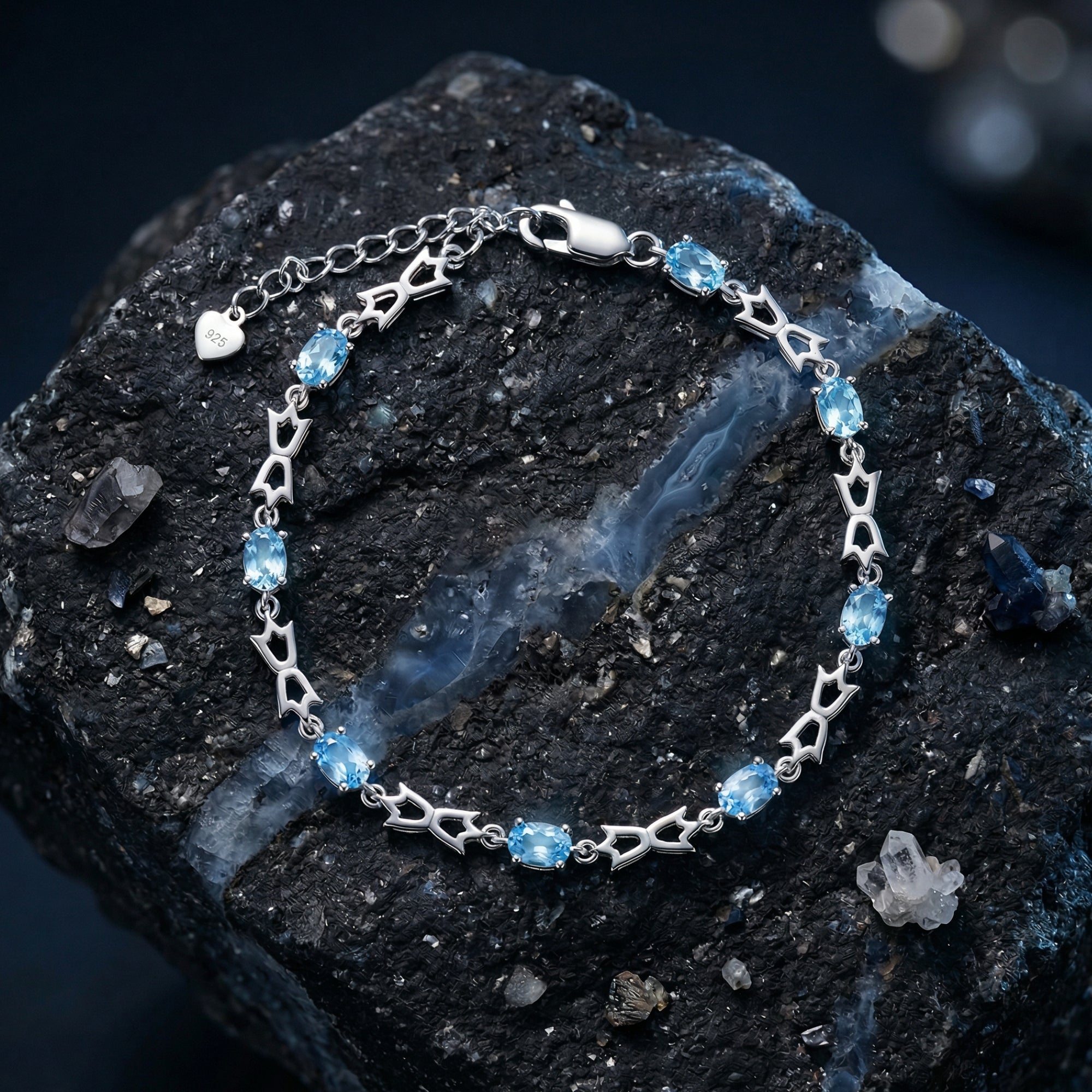 Silver Aquaria bracelet with oval-cut blue topaz stones on a dark rock surrounded by raw crystals.