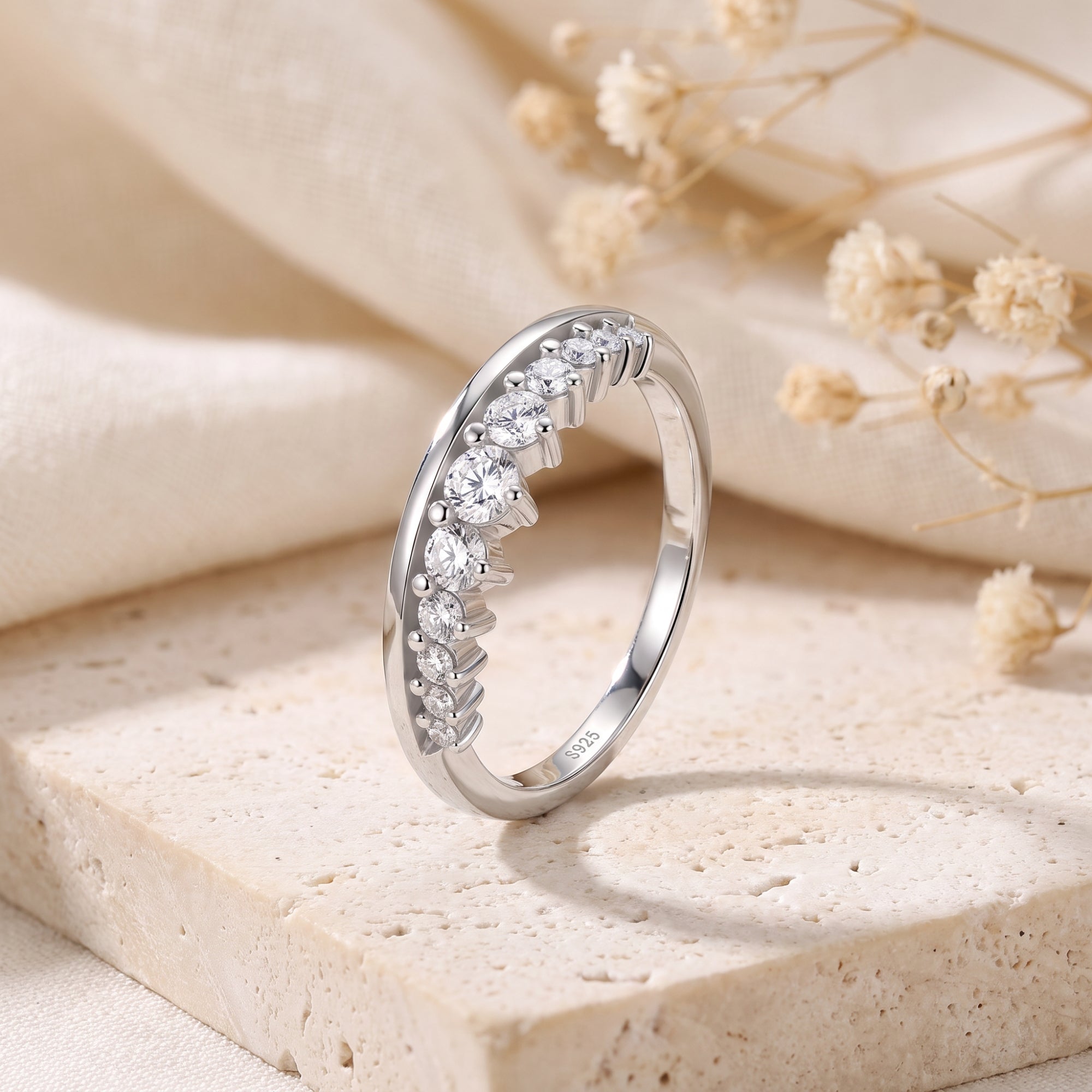 Graduated silver curved ring with round cubic zirconia on a stone surface.