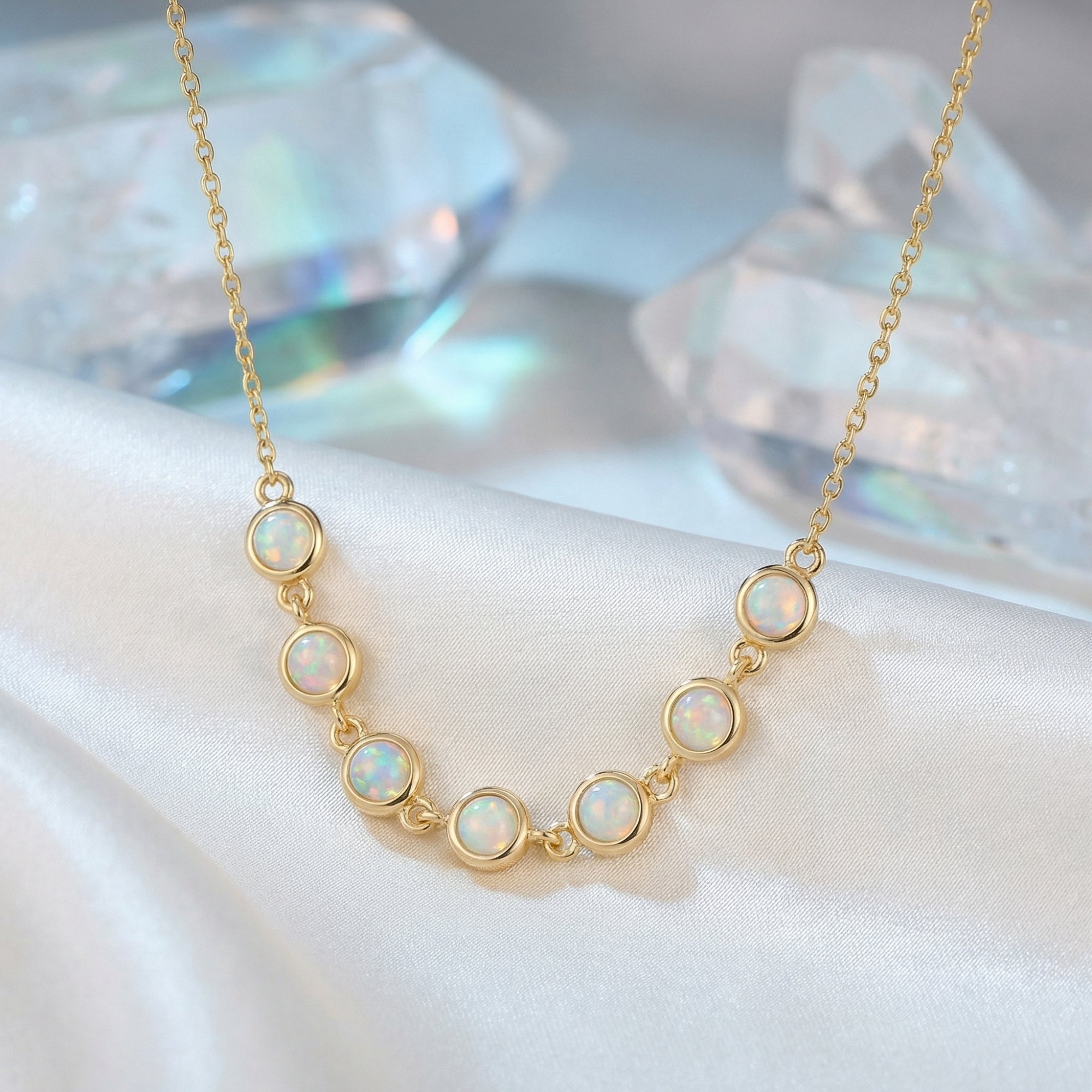 Gold-tone Lumina necklace with seven round white opals, styled on white silk with crystal props.