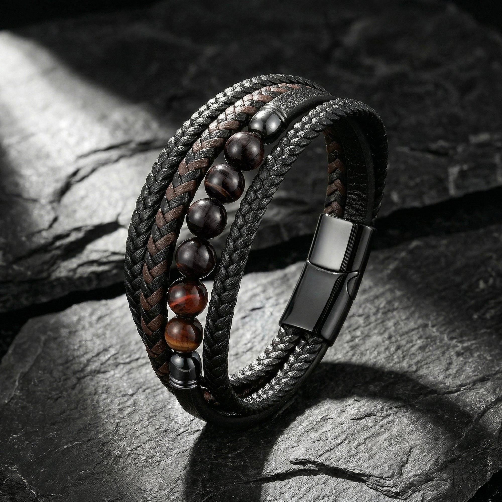 Men's black braided leather bracelet with red tiger's eye beads and black steel clasp on a textured stone surface.
