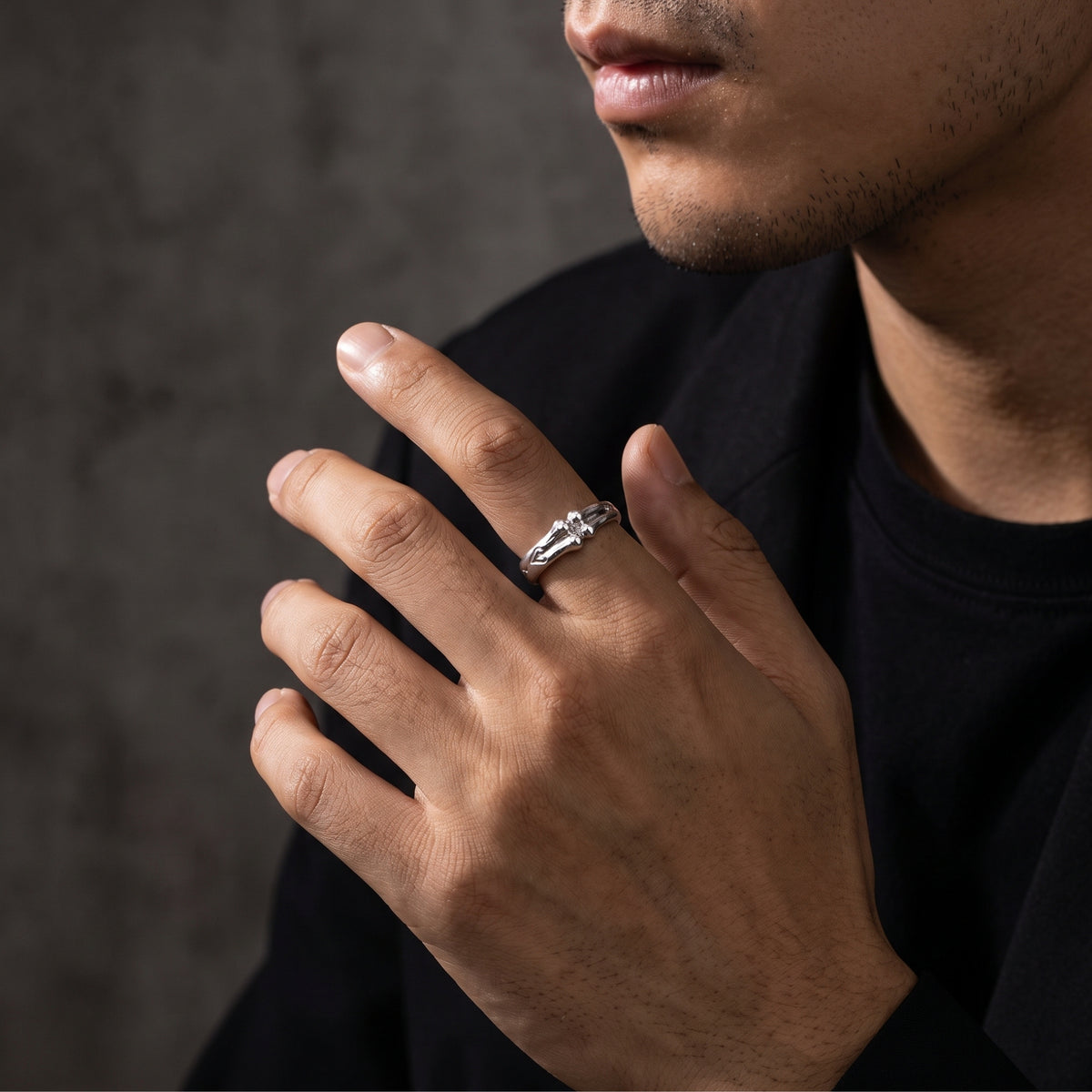 Man wearing the silver bone-motif open band ring on his middle finger against a dark backdrop.
