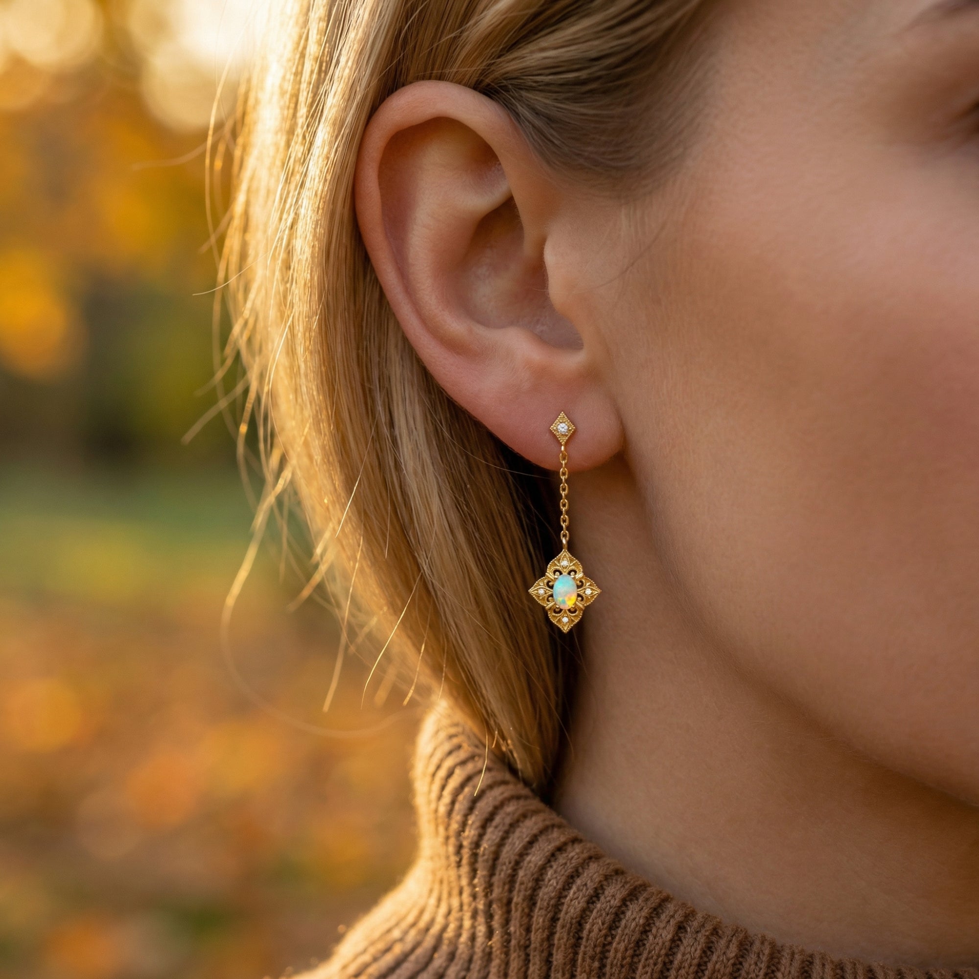 Model wearing a gold-tone filigree drop earring with a white opal stone in an outdoor setting.