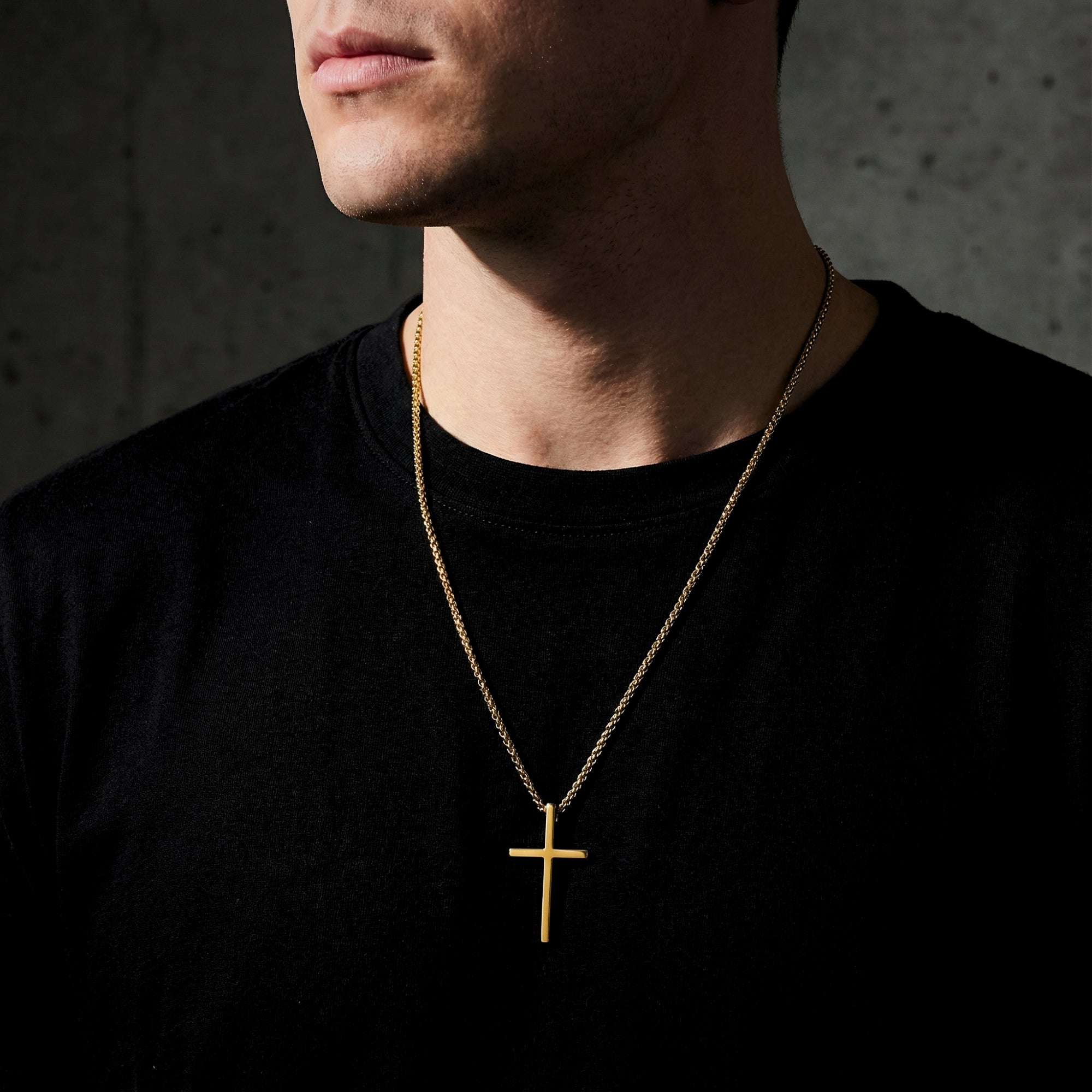 Front view of a man wearing the gold tone stainless steel Devotion Cross necklace over a black t-shirt.