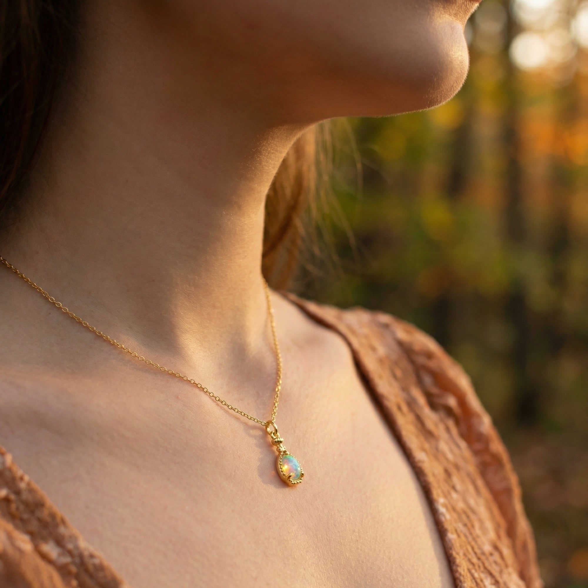 Model wearing the gold-tone Lumira pear cut natural opal necklace against a blurred outdoor autumn background.