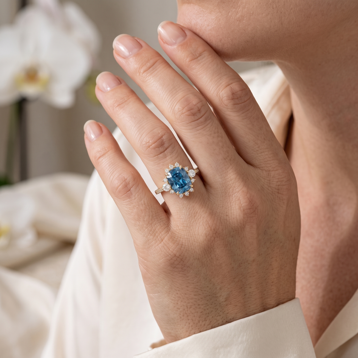 A woman wearing a rose gold cushion-cut blue moissanite engagement ring with a diamond halo cluster.