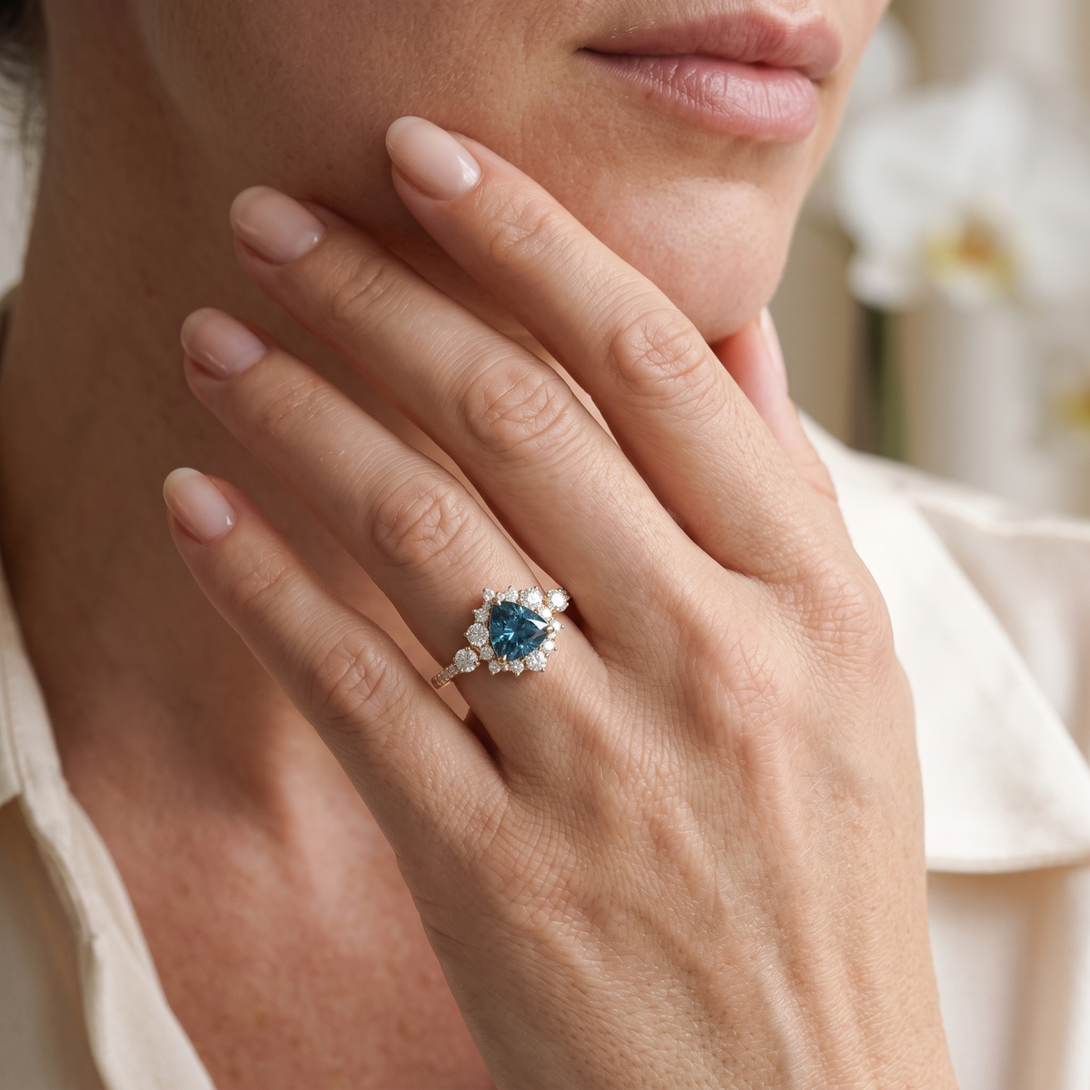 Model wearing a rose gold trillion-cut blue moissanite halo ring on her hand near her chin.
