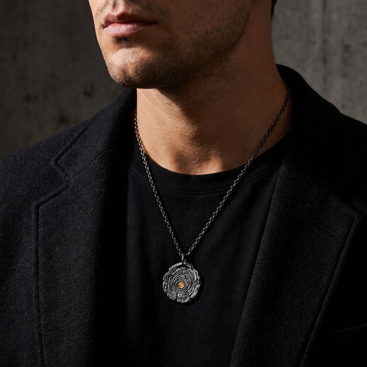 Man wearing the growth ring pendant necklace with a black T-shirt and dark blazer.