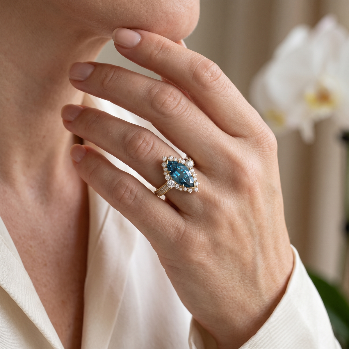 A woman wearing a yellow gold marquise blue moissanite halo ring on her finger.