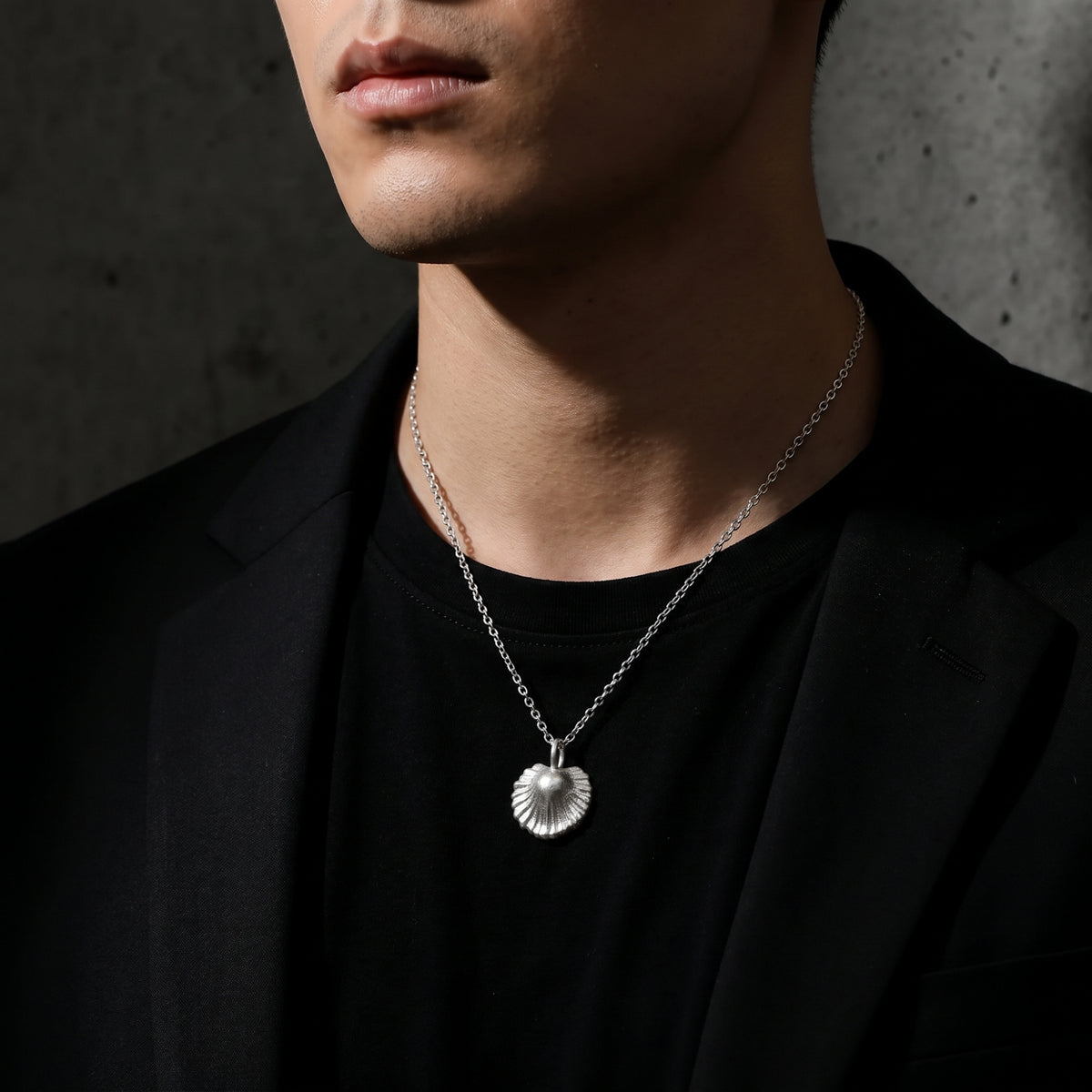Man wearing the silver scallop shell necklace with a black T-shirt and jacket.