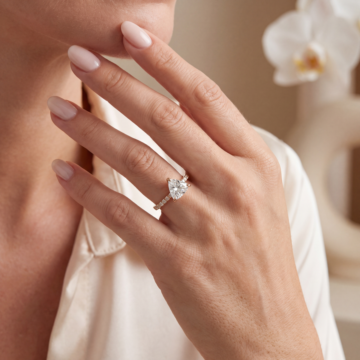 Model wearing a yellow gold trillion-cut moissanite engagement ring on hand near face.