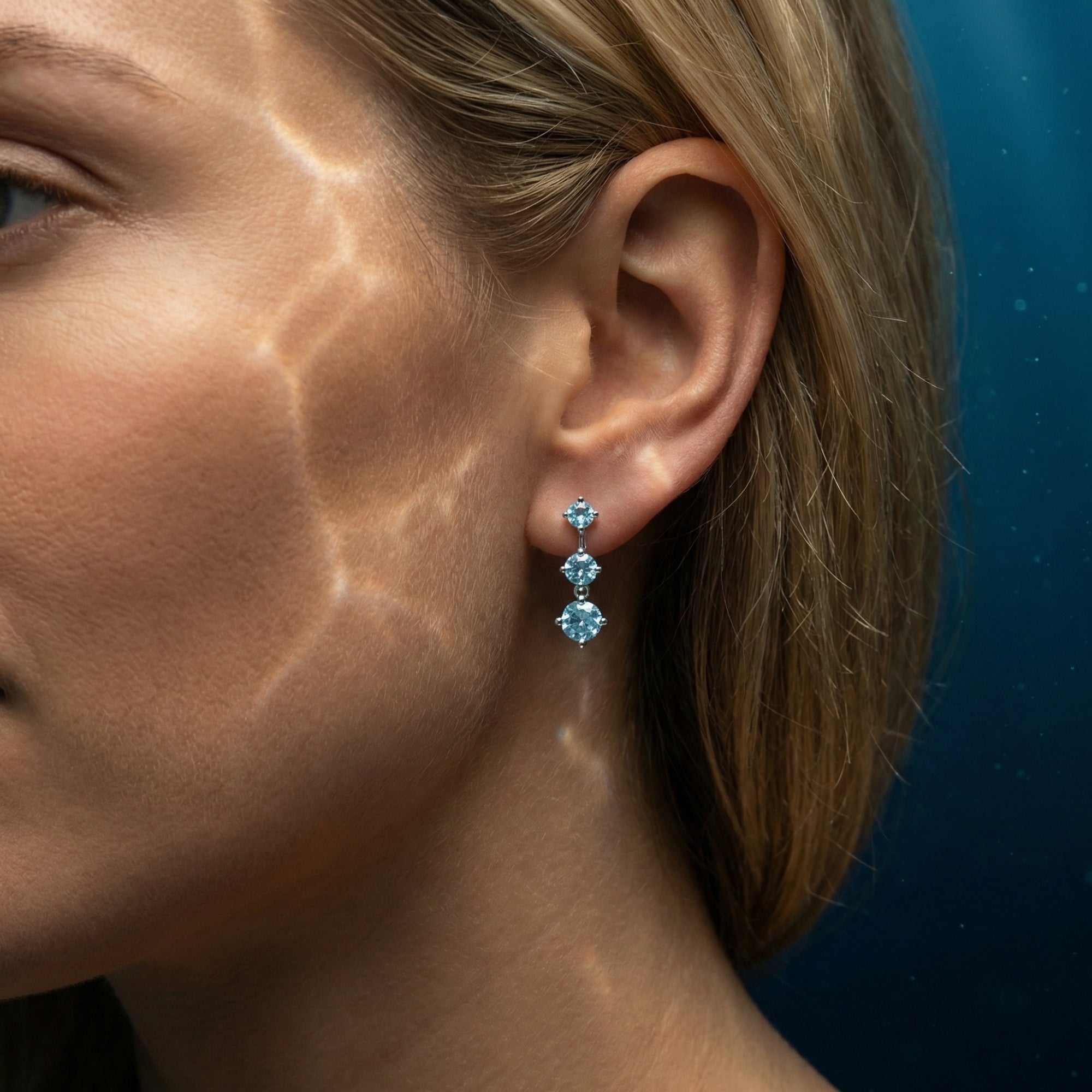 Woman wearing a graduating trio of round aquamarine drop earrings in platinum with ocean-like light reflections.
