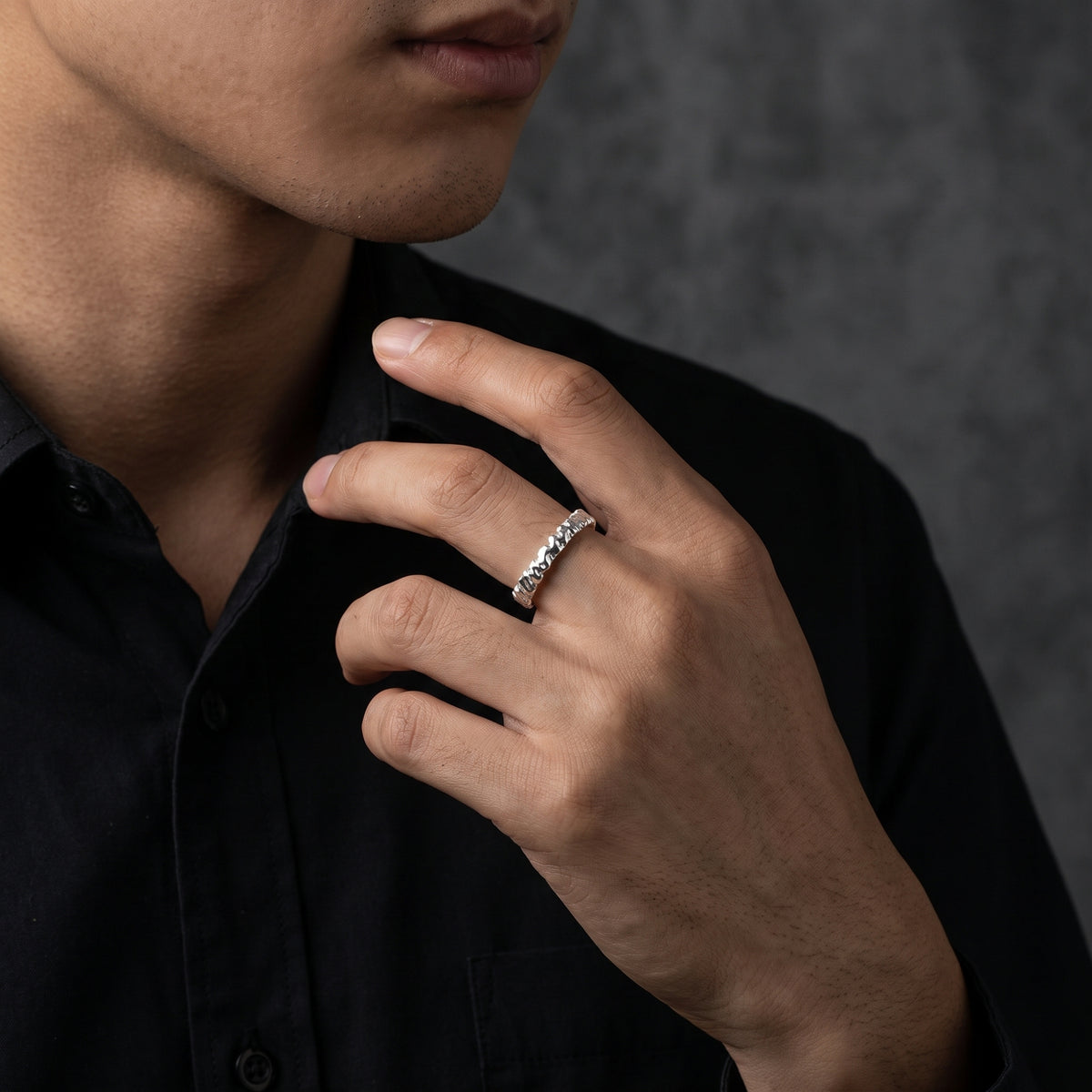 Silver carved open-band ring worn on a man's ring finger against a black shirt.