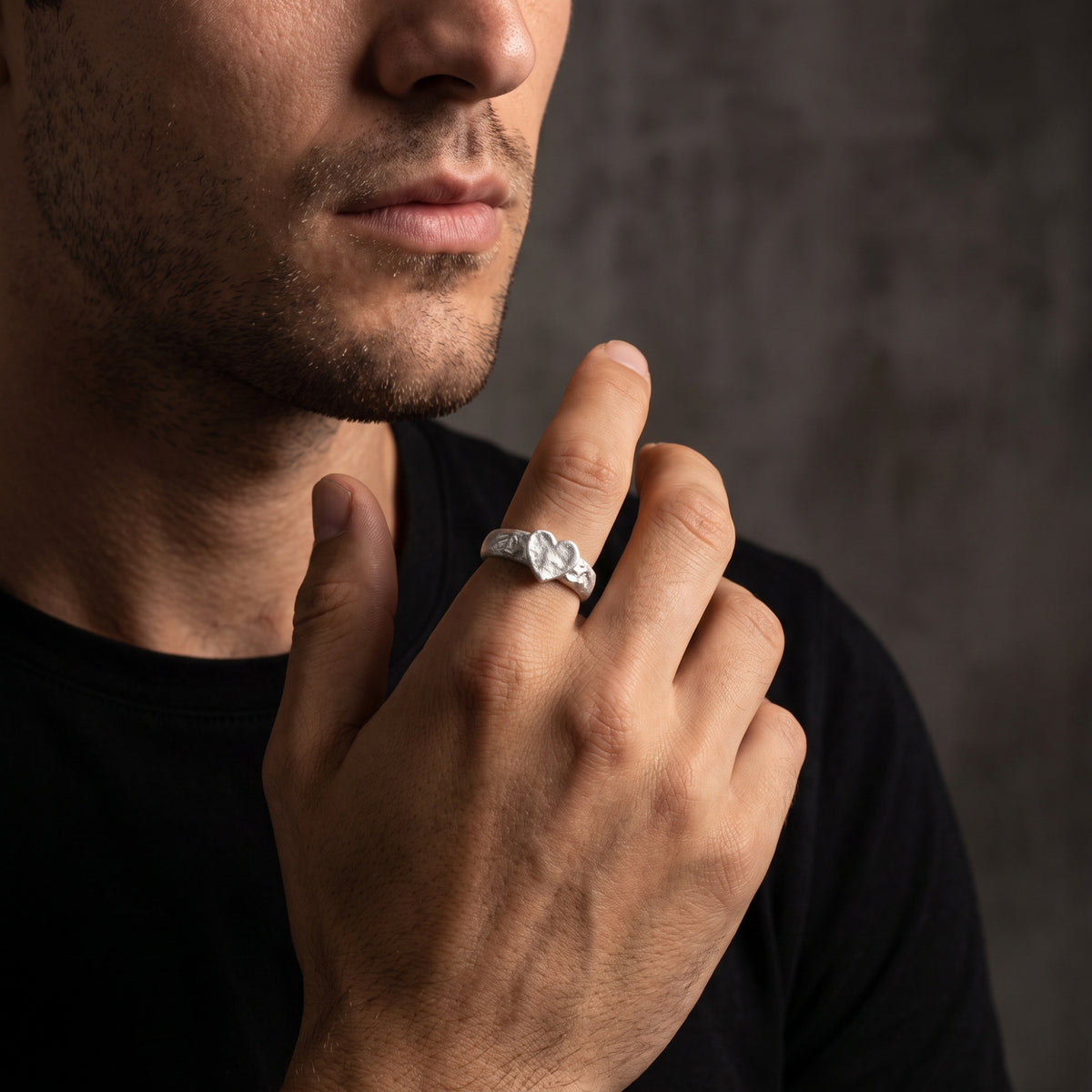 Man wearing the hammered heart ring on his index finger with his hand raised near his face.