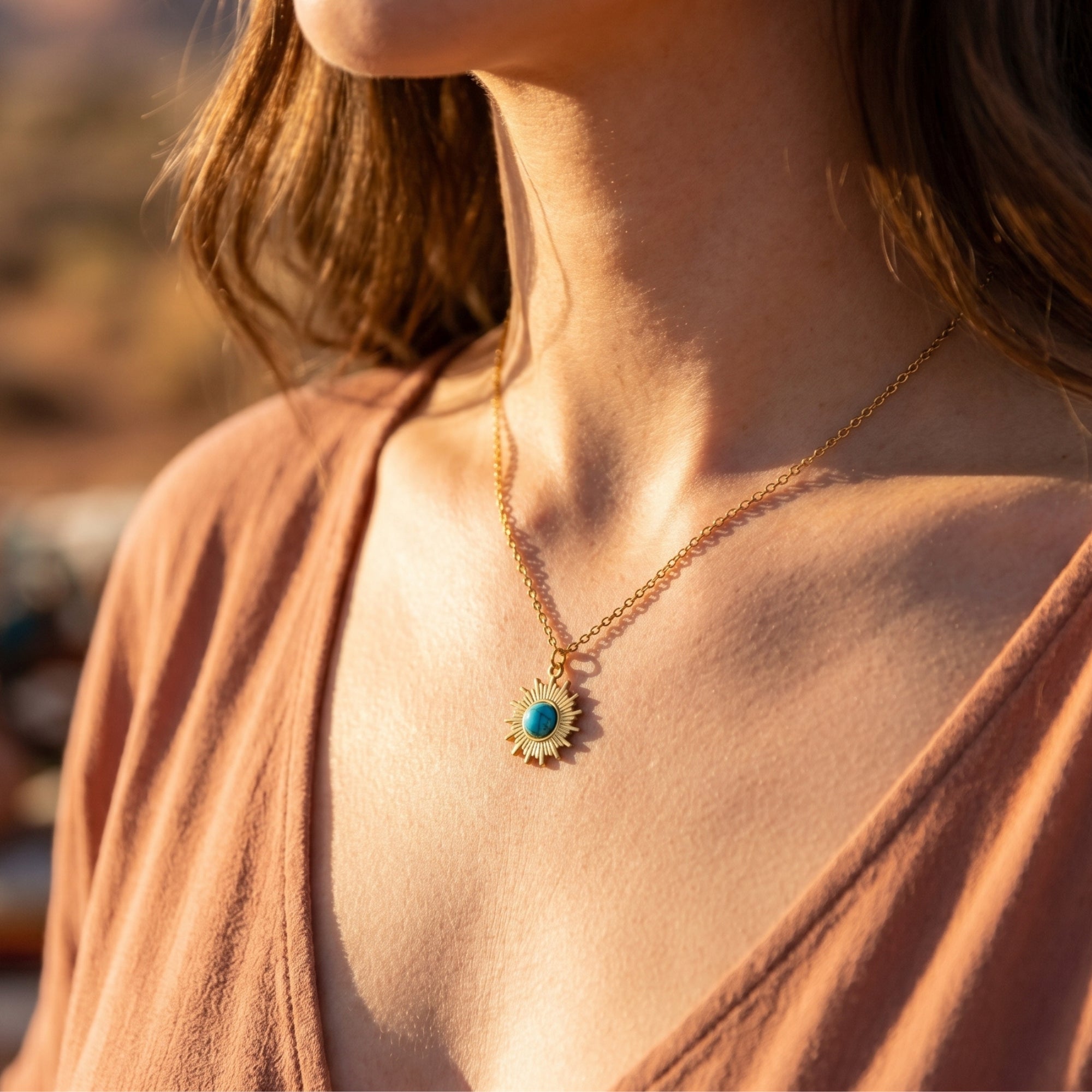 Gold finish sunburst necklace with a turquoise stone worn by a model in natural sunlight.