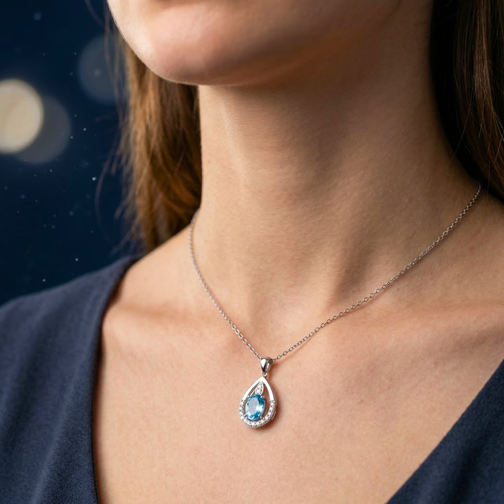 Side view of a model wearing the silver Coriana necklace with an oval cut blue topaz teardrop pendant.