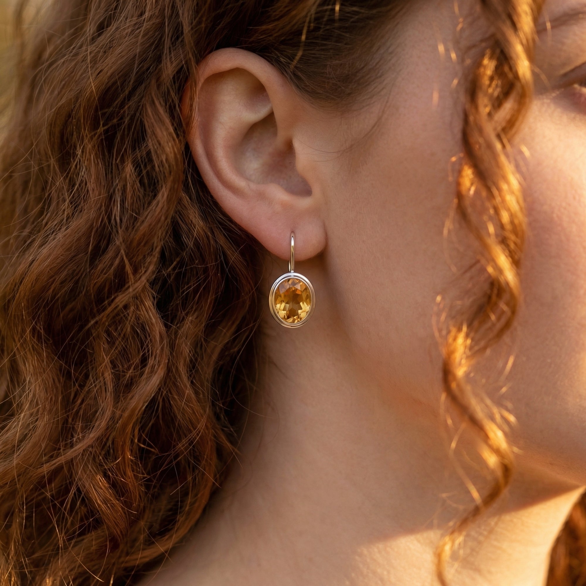 Model wearing a sterling silver drop earring featuring a faceted oval natural citrine gemstone.