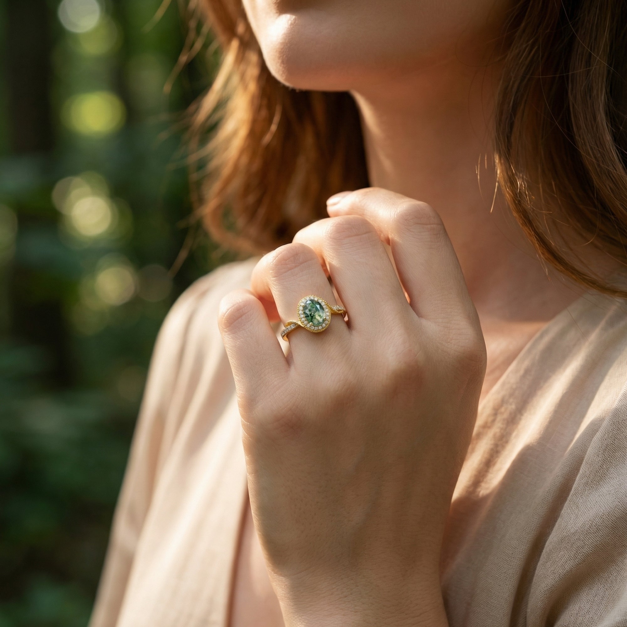 Model wearing a halo oval cut moss agate gold ring on her finger with a natural forest background.