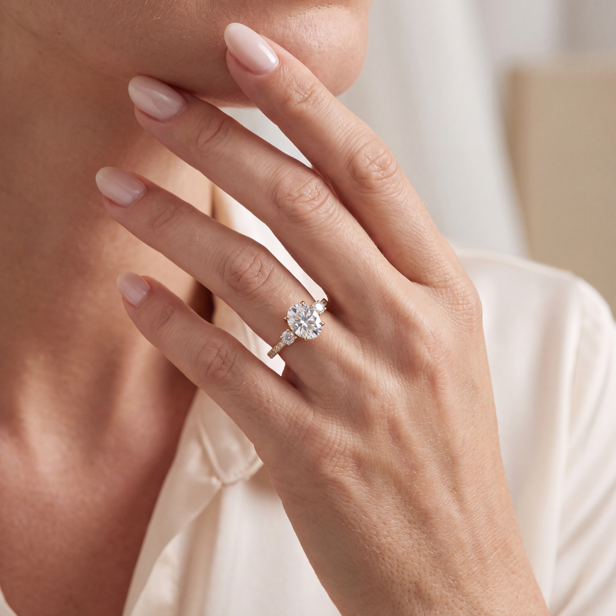 Model wearing the yellow gold oval moissanite three-stone ring on her finger while posing near her face.