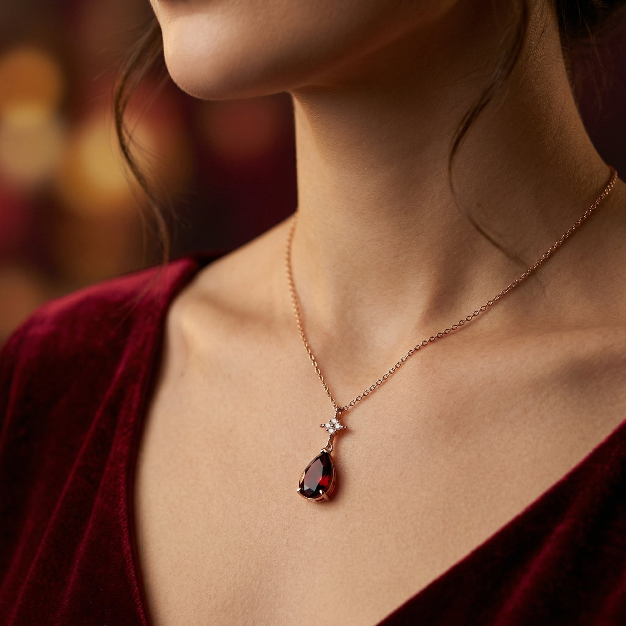 Side view of a model wearing the 3.4CT pear-cut garnet pendant in 18K rose gold with a red velvet dress.