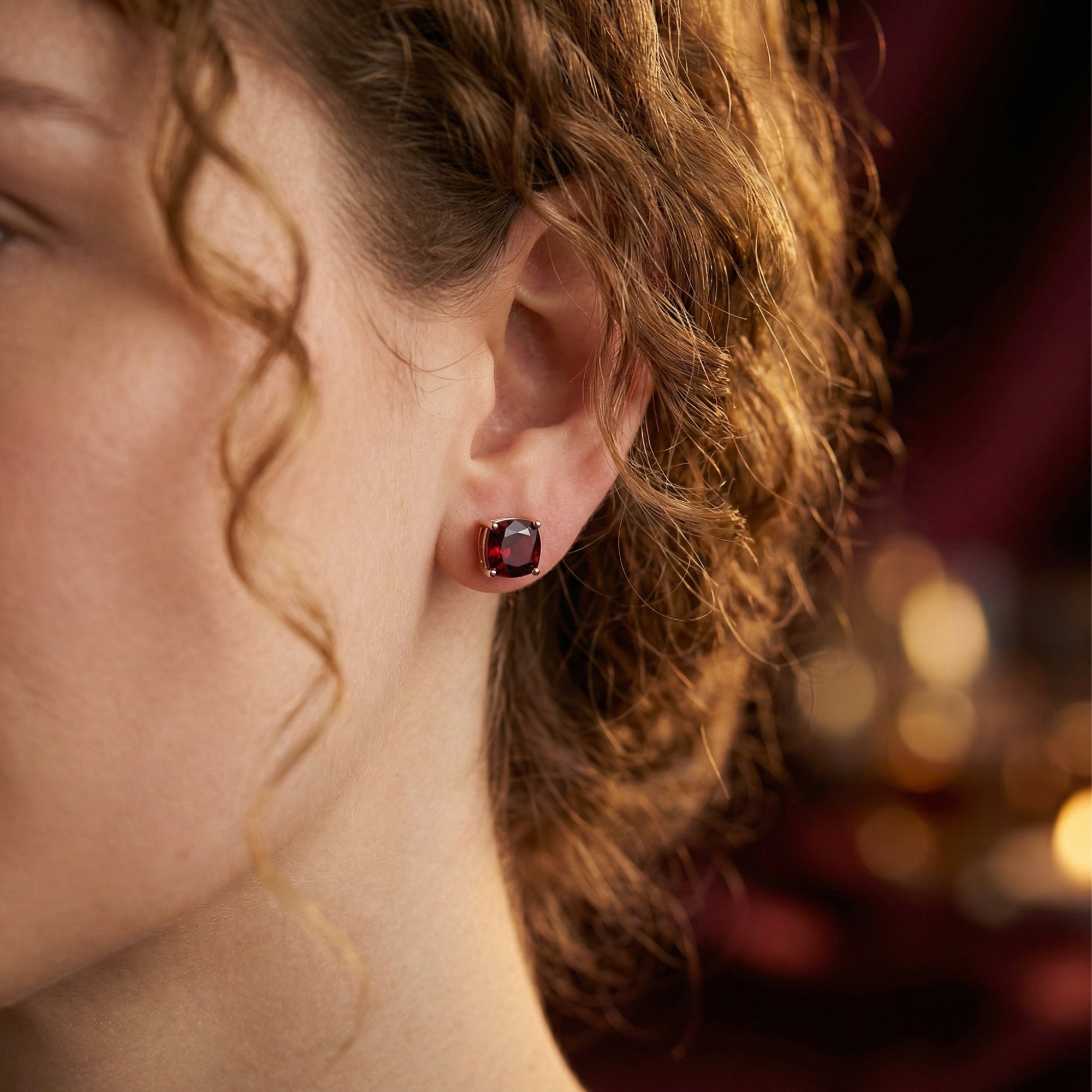 Cushion cut red garnet stud earring in 18K rose gold shown on a model's ear.