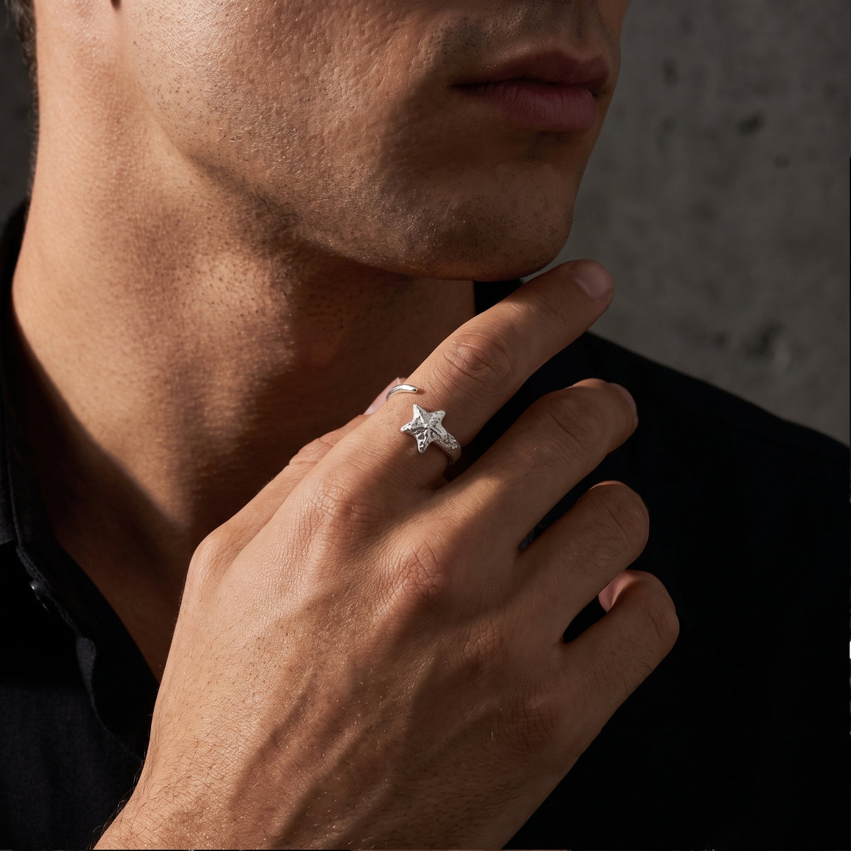Man wearing a silver star open ring while holding his hand near his chin.