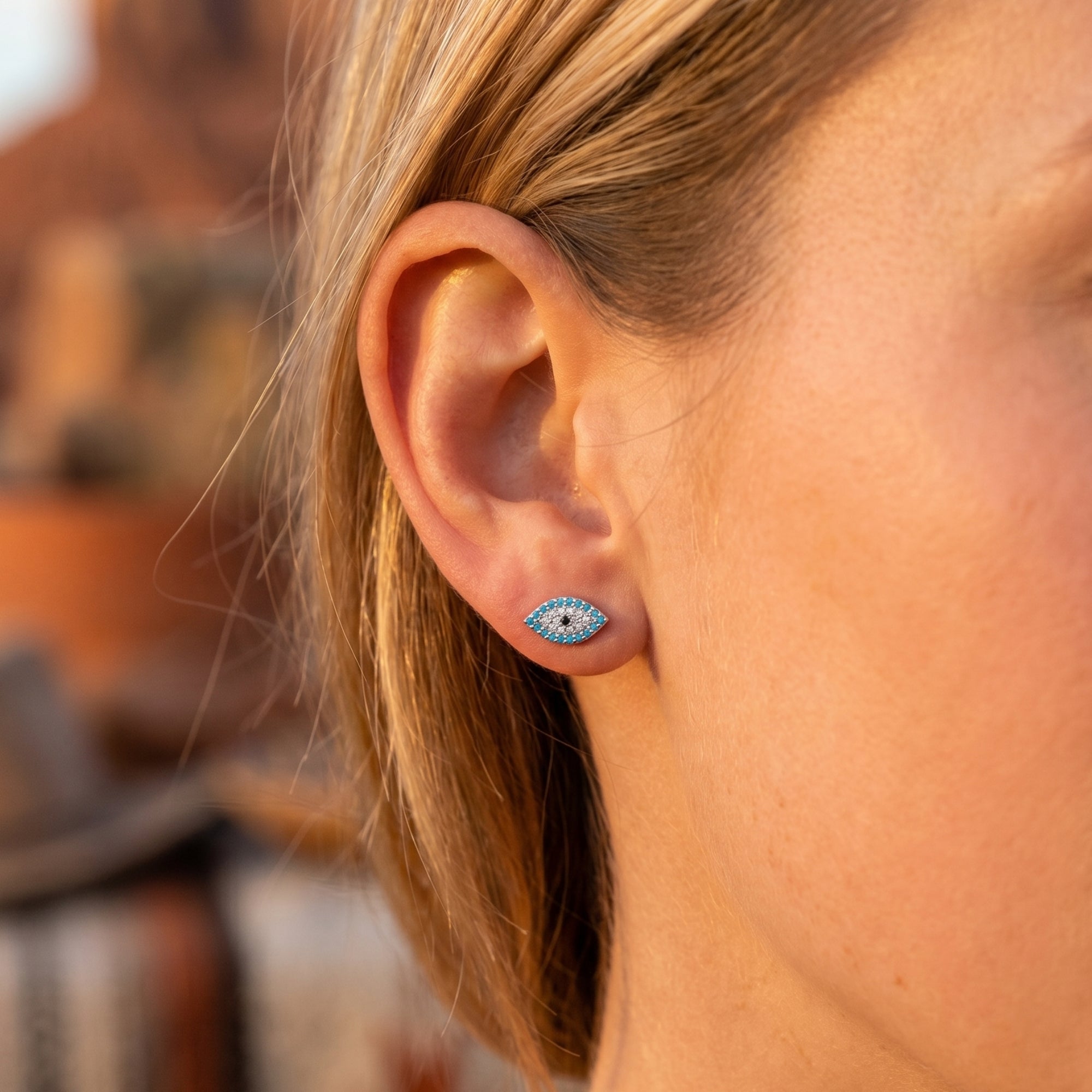 Woman wearing a silver turquoise evil eye stud earring with simulated diamonds in a Southwestern-inspired style.