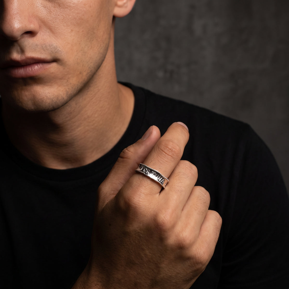 Model wearing the silver Fortuna engraved ring on his index finger against a dark background.