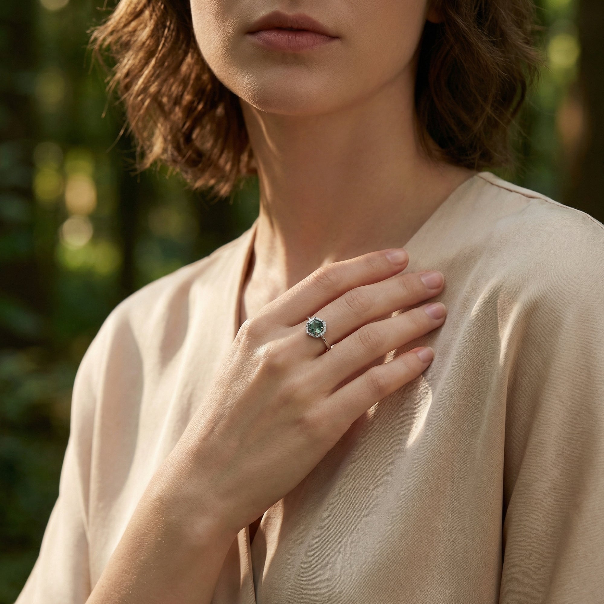 Model wearing a hexagonal moss agate halo ring in sterling silver on her hand in a forest setting.
