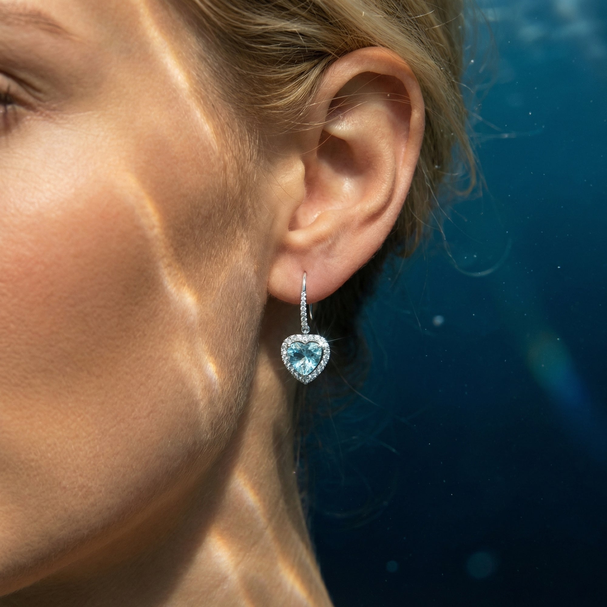 Close-up of a woman wearing a platinum heart-cut aquamarine drop earring with a diamond halo.