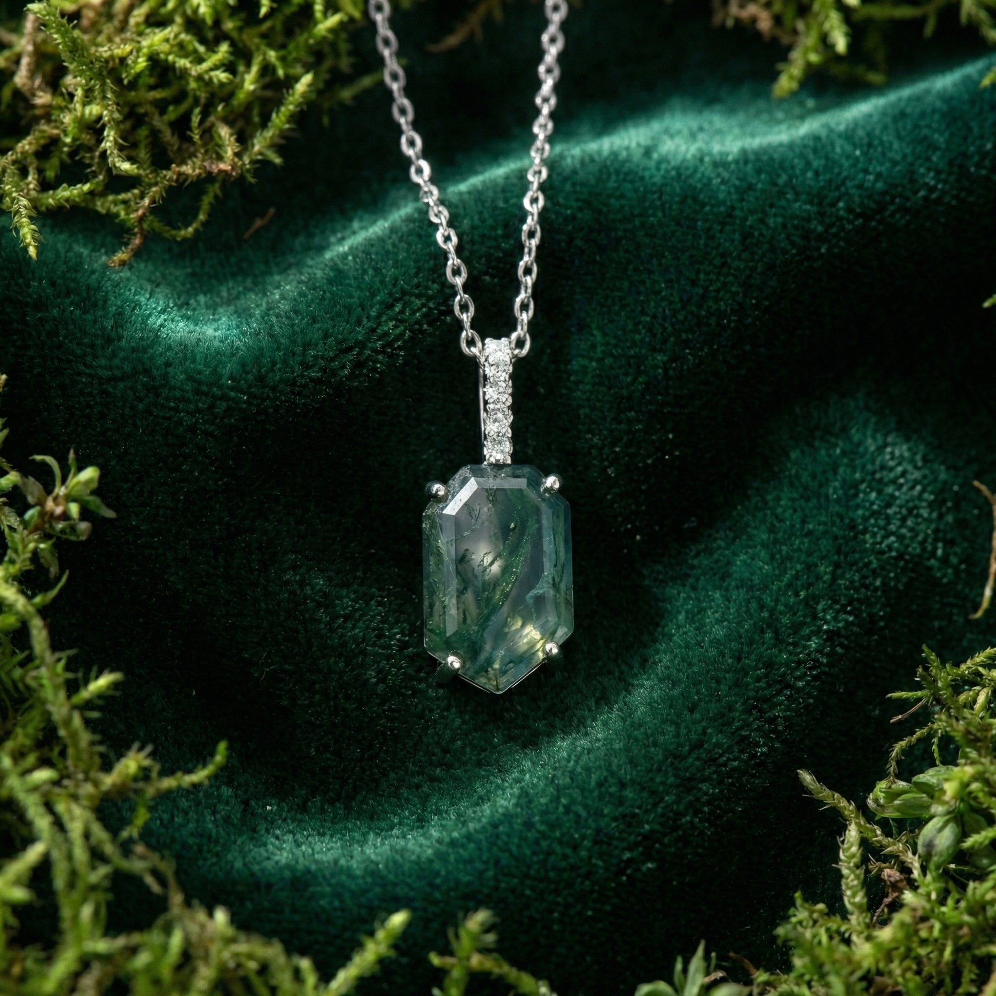 Top-down view of a coffin cut moss agate column pendant in sterling silver, set against green velvet and forest moss.