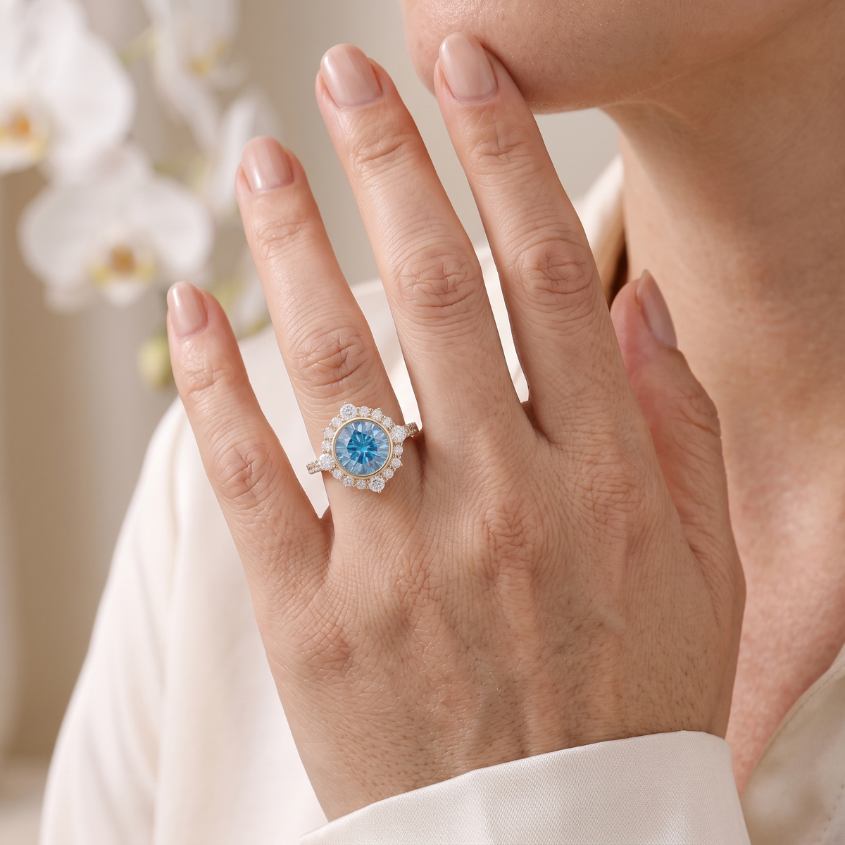 Round blue moissanite halo engagement ring in rose gold worn on a woman's hand.