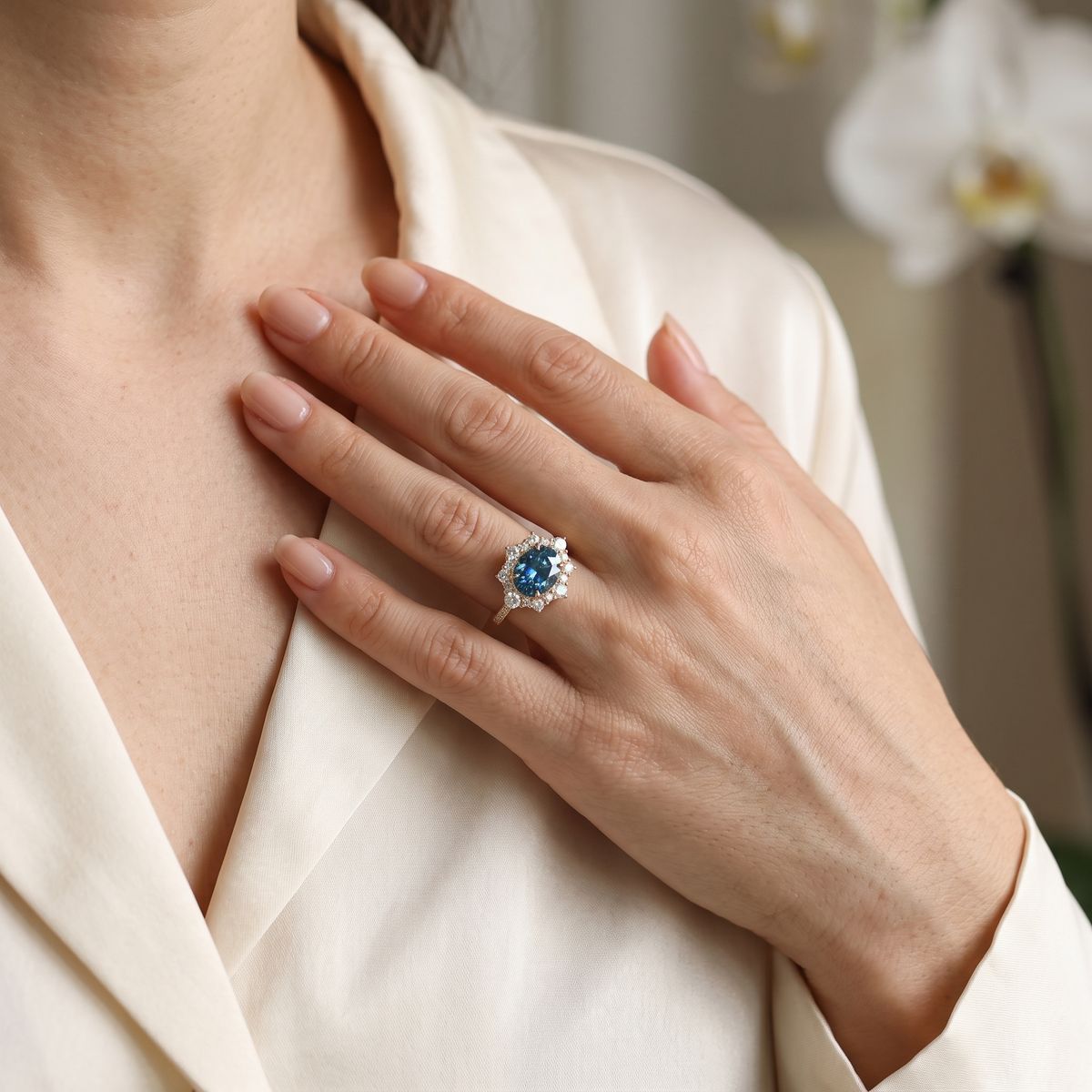 Model wearing a rose gold oval blue moissanite halo ring against a silk blouse.