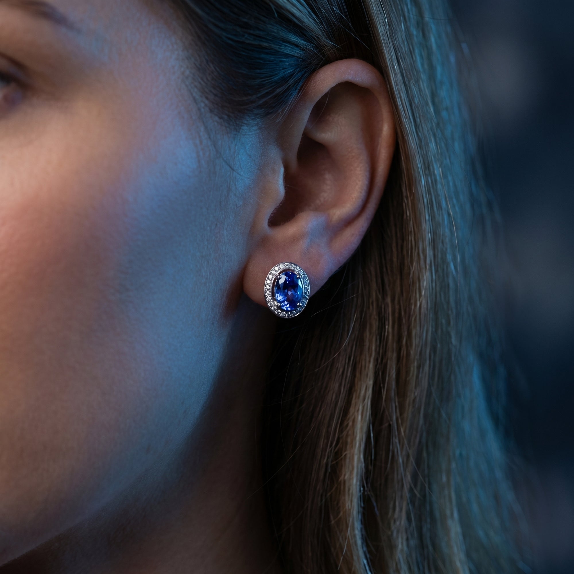 Woman wearing an oval natural tanzanite and diamond halo stud earring in 18K white gold.
