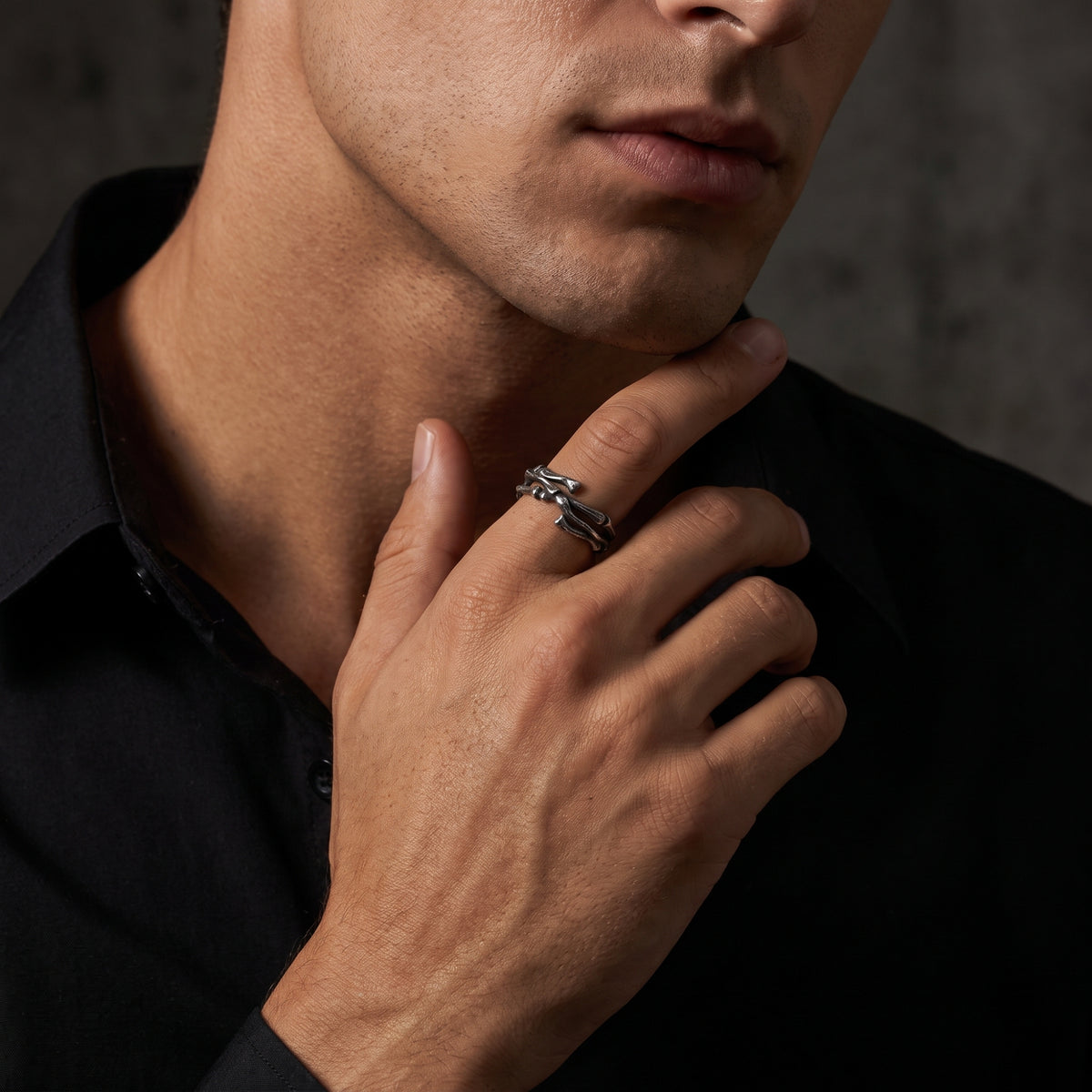 Model wearing the oxidized silver skeletal open band ring on an index finger raised toward his chin.