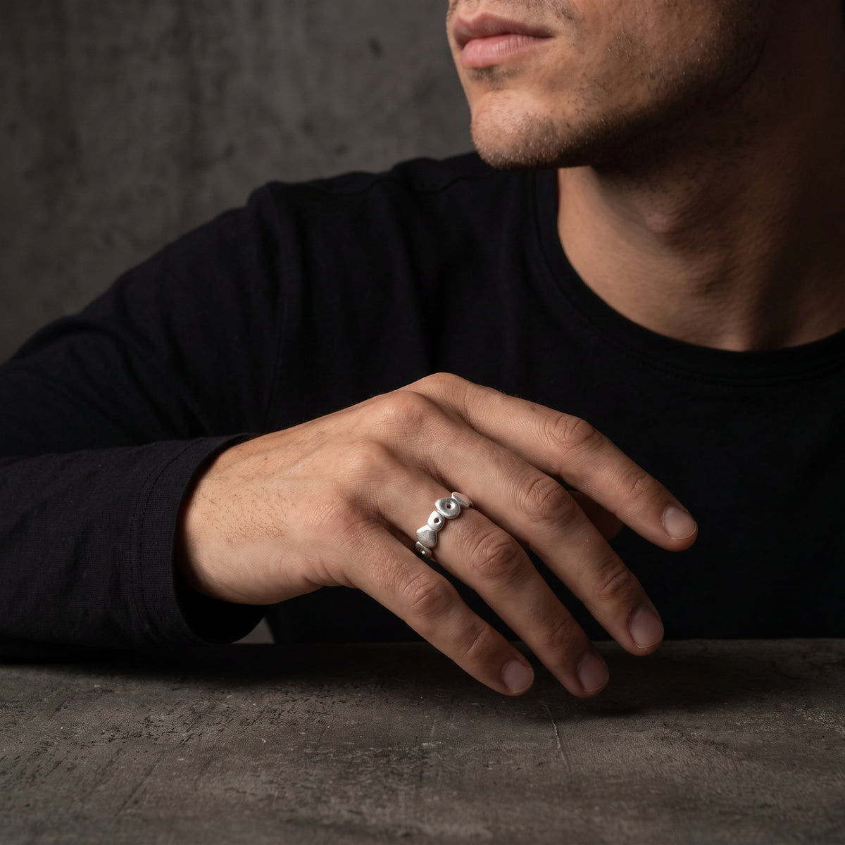 Man wearing the silver pebble open-band ring on his ring finger, with his hand resting on a dark tabletop.