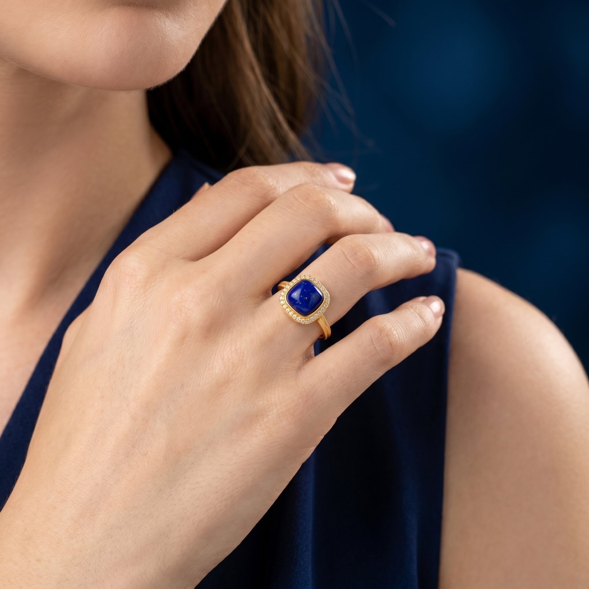 Model wearing the gold Amarys ring with a square natural lapis lazuli stone and halo setting on her finger.