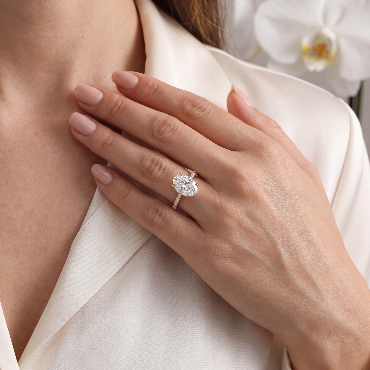 A woman wearing a gold oval moissanite engagement ring with a pavé band on her finger.