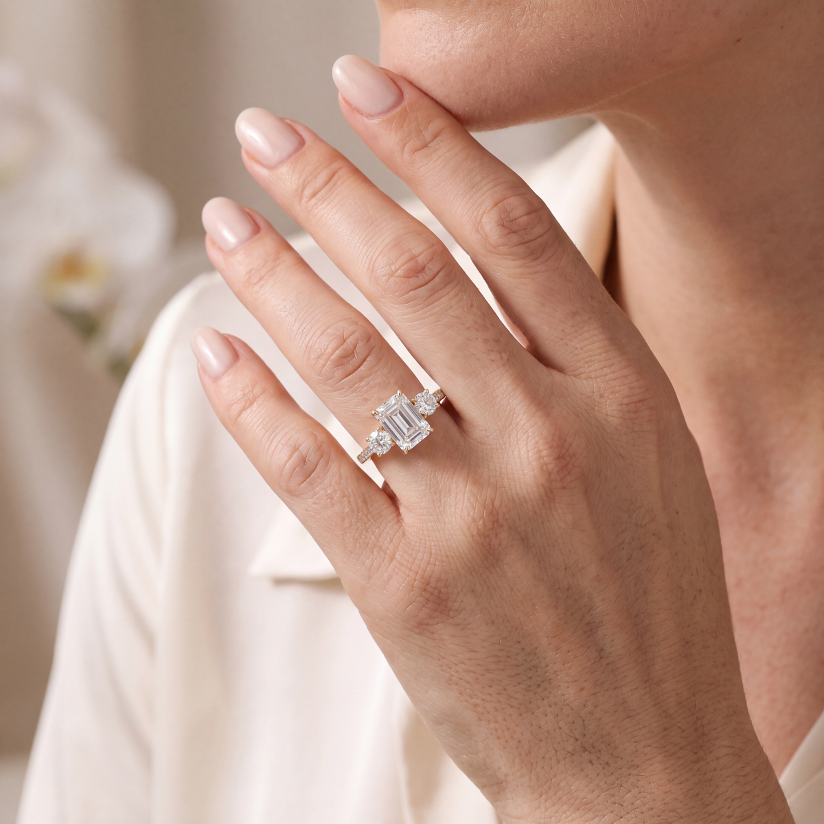 Model wearing a yellow gold emerald cut three-stone moissanite ring on her finger.
